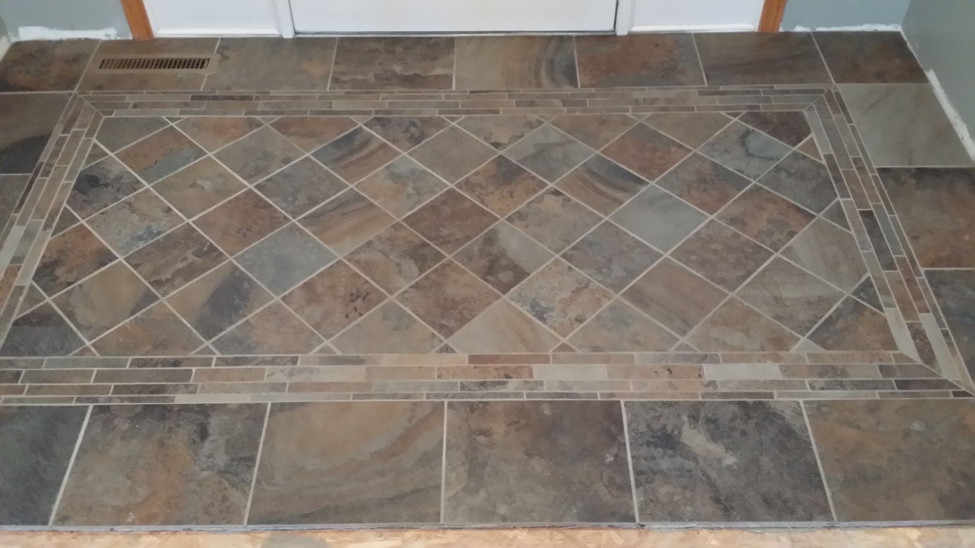 Slate-tile entryway with a diamond-patterned center framed by a mosaic border.