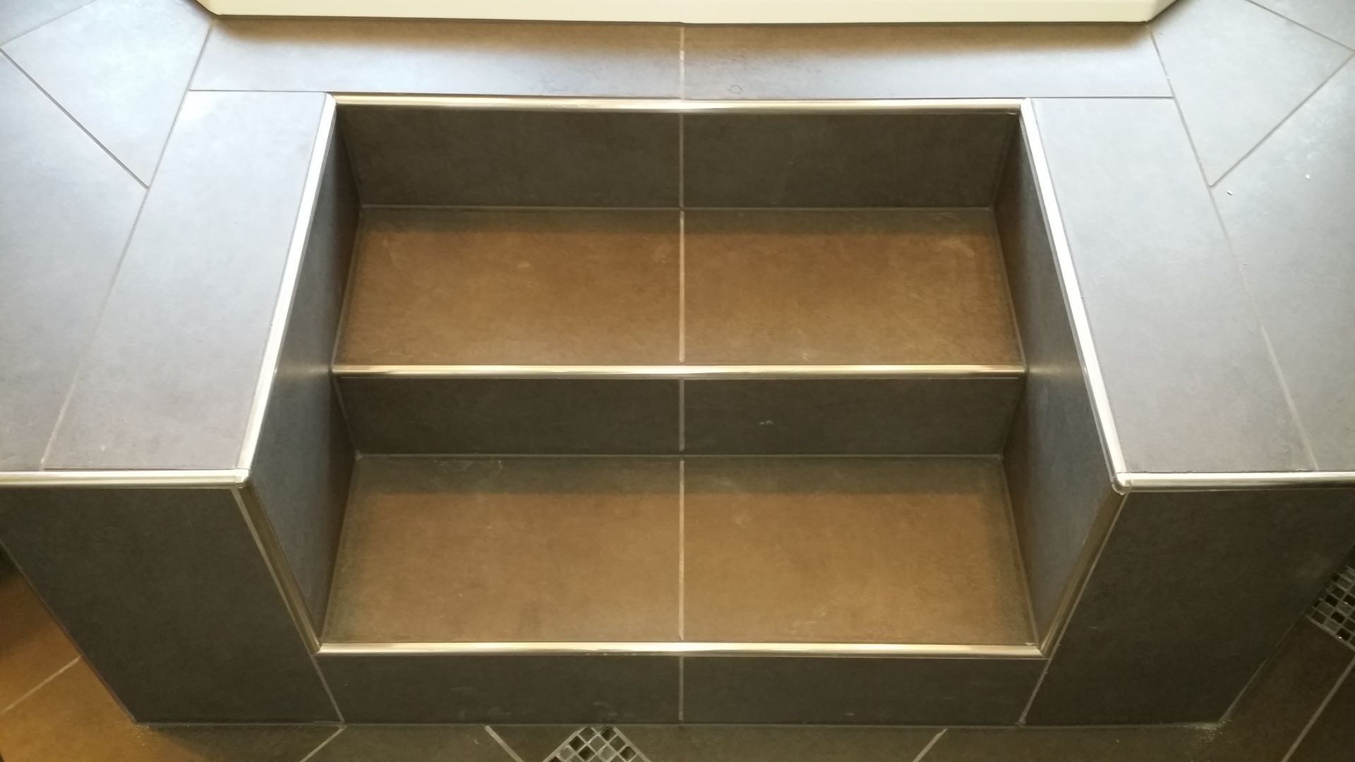 Tile steps in a bathroom, grey tiled walls and a grey-brown interior.