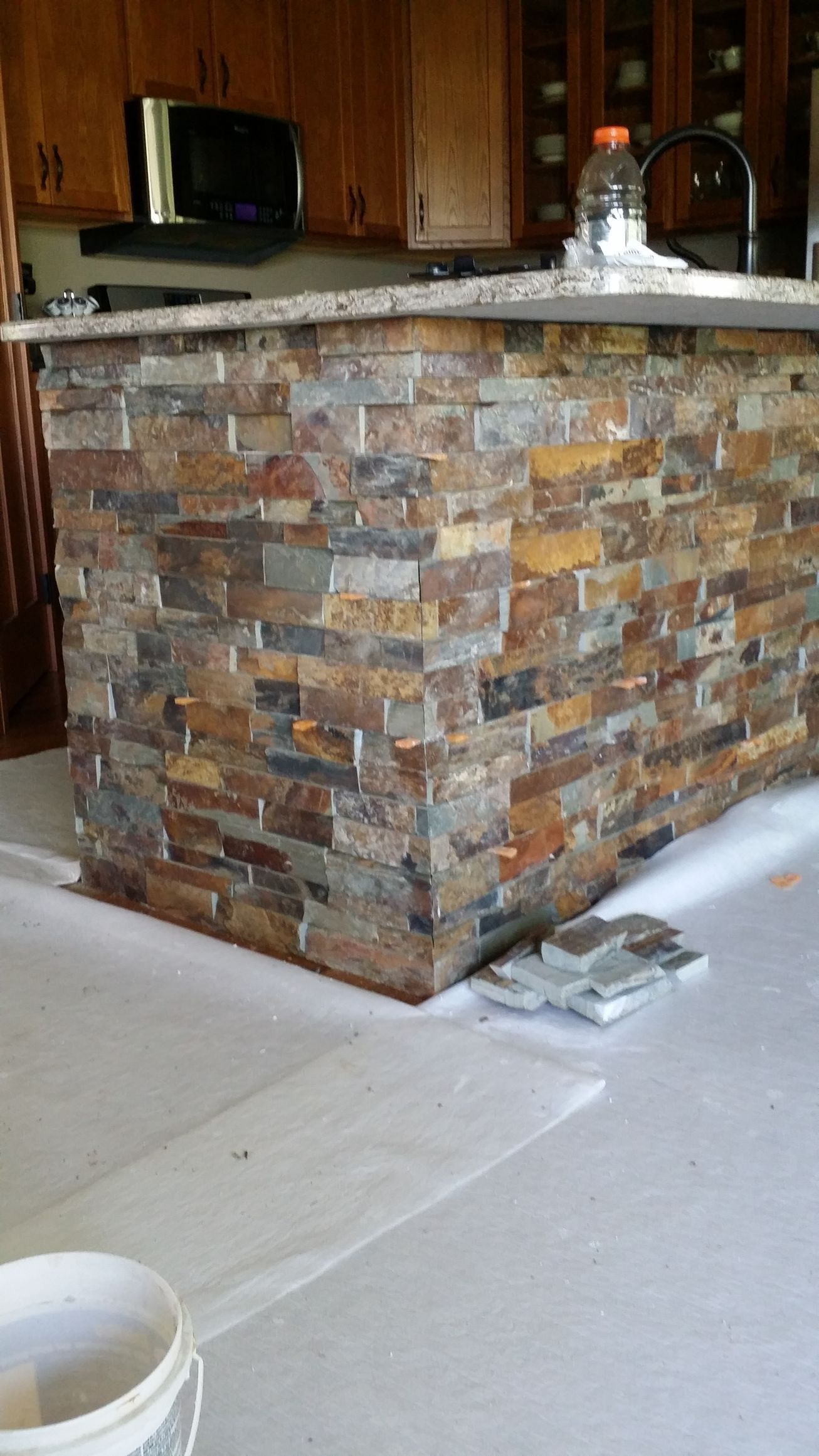 Stone-covered kitchen island, brown, gray, and orange tiles, with granite countertop, under construction with materials nearby.