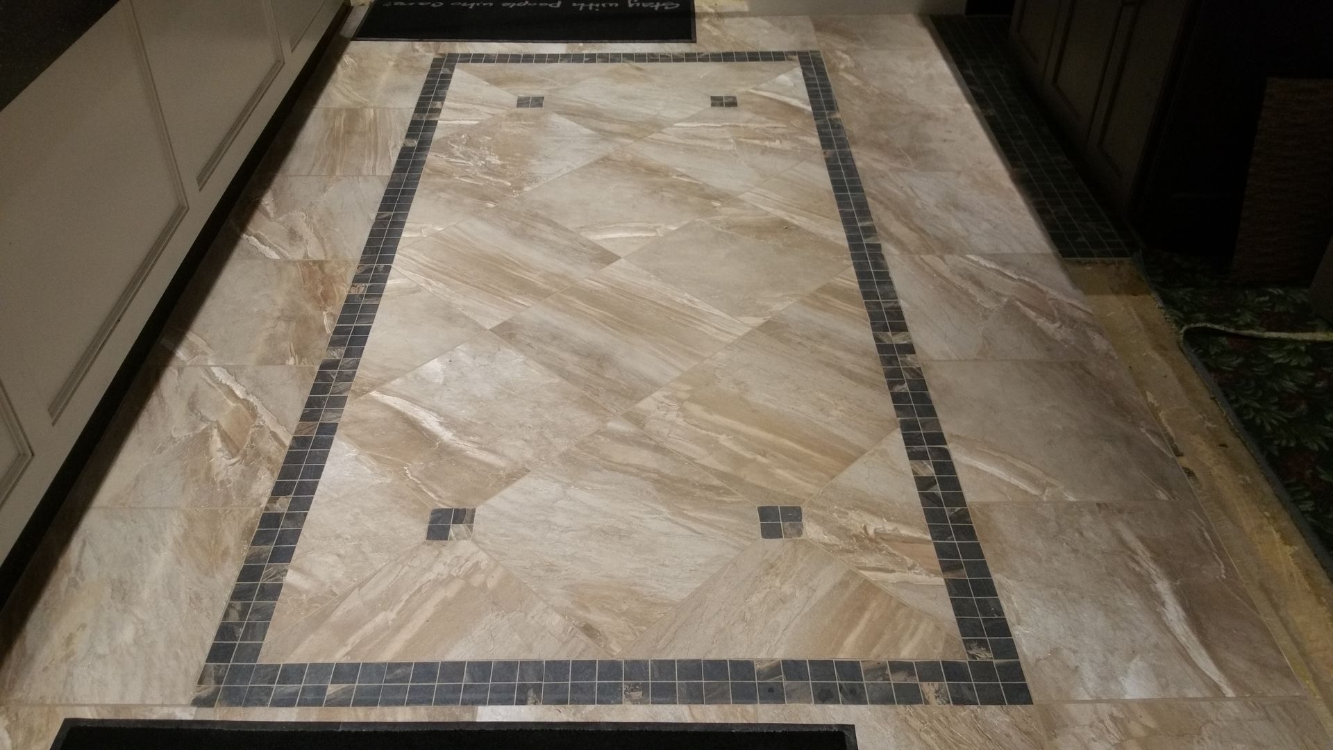 Tiled kitchen floor with a rectangular dark border and scattered dark squares.