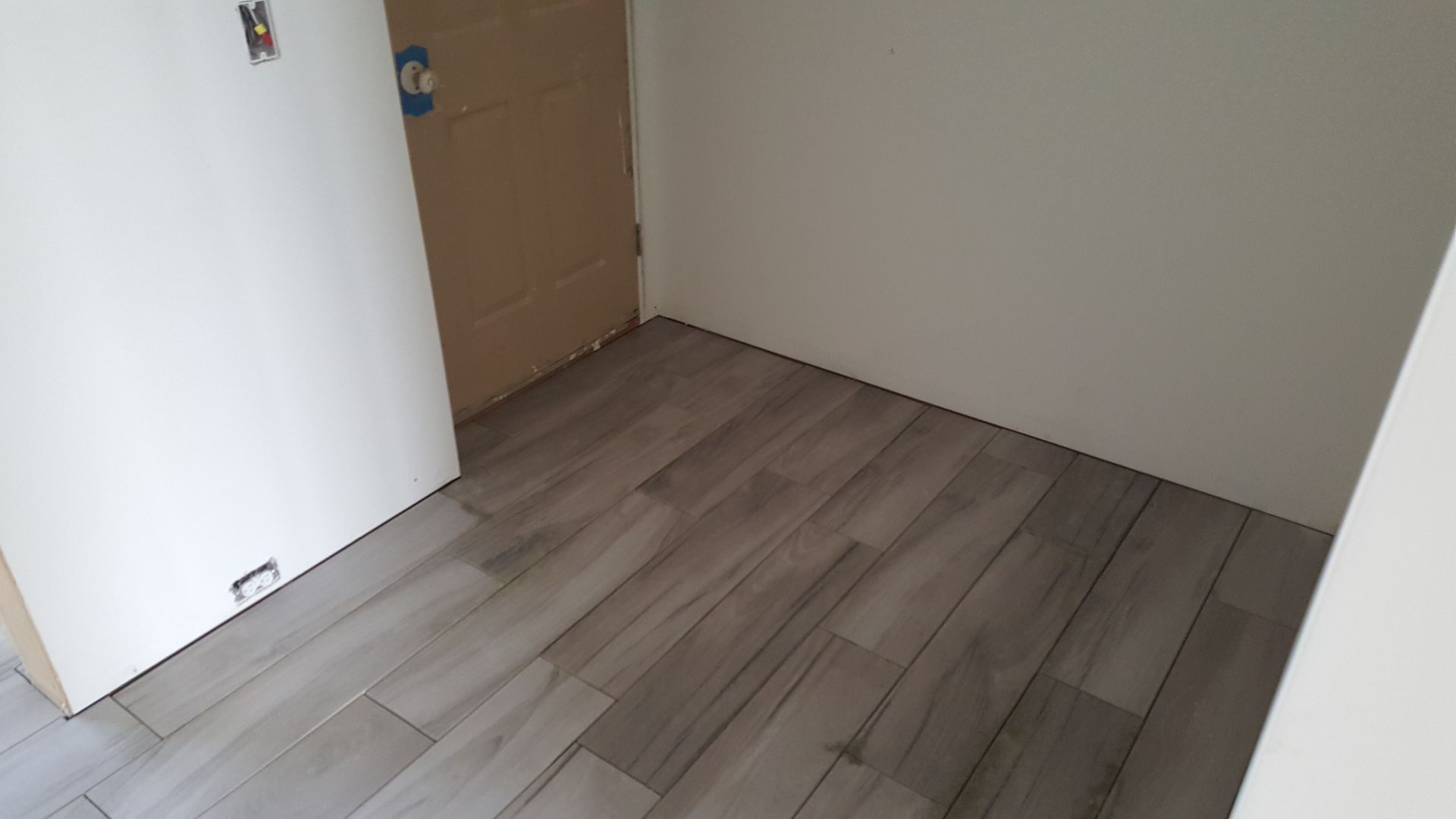 A small room with wood-look tile flooring and beige walls; a door is visible.