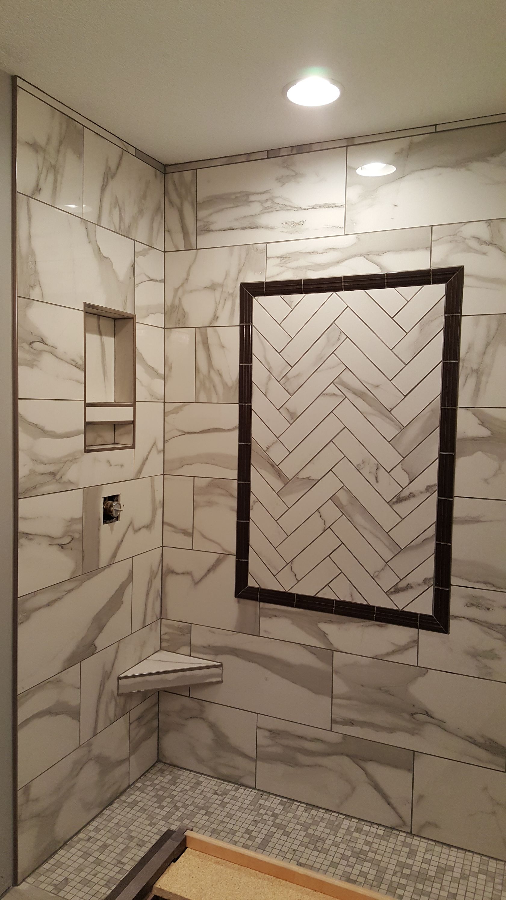 Bathroom with marble-patterned tile walls, herringbone tiled niche, and pebble floor.