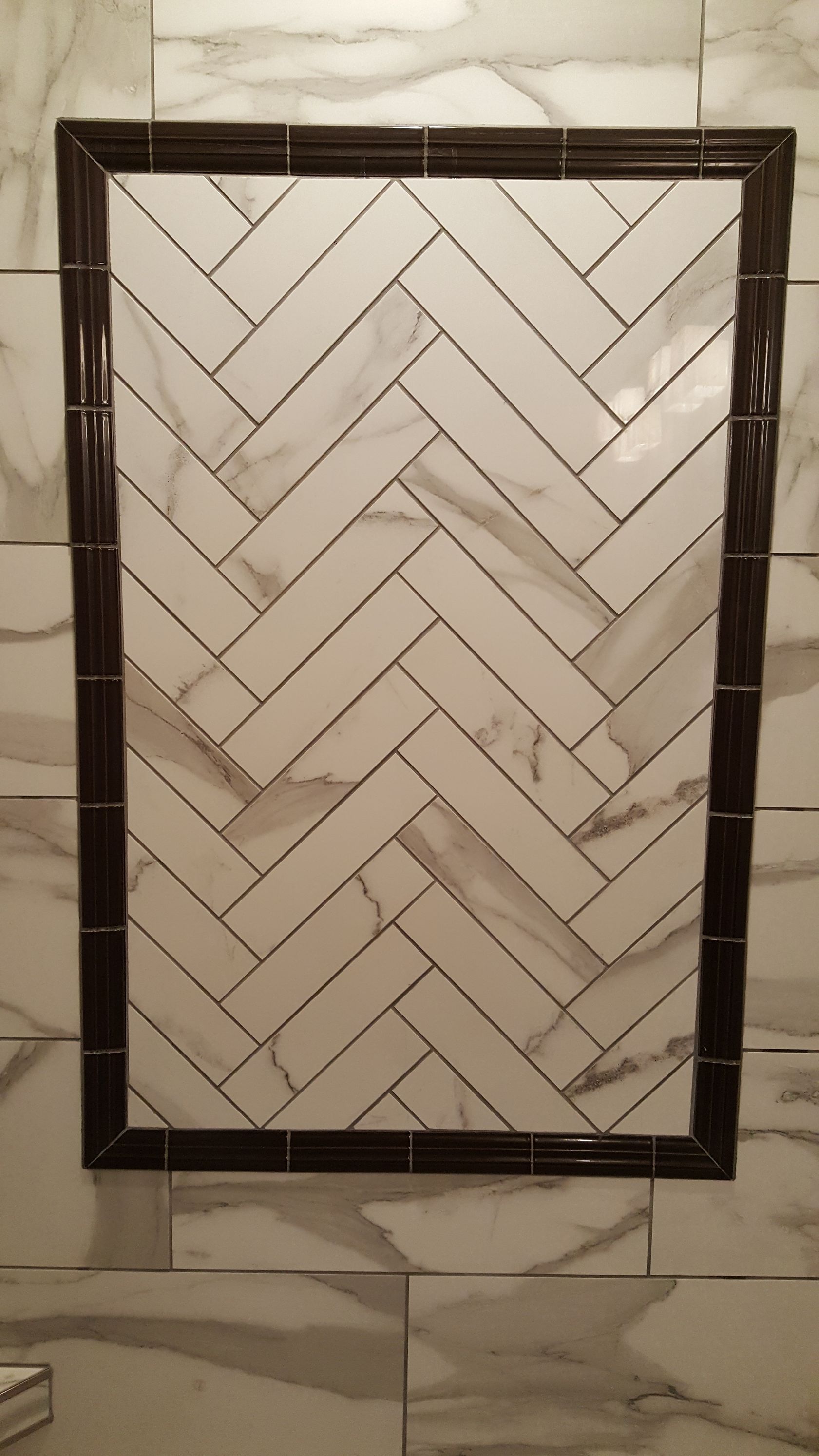 Shower niche with herringbone white tile, framed by dark brown trim.