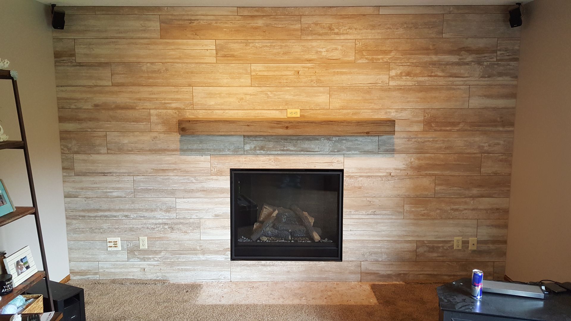 Fireplace with textured stone wall, wooden mantel, and speakers; neutral tones.