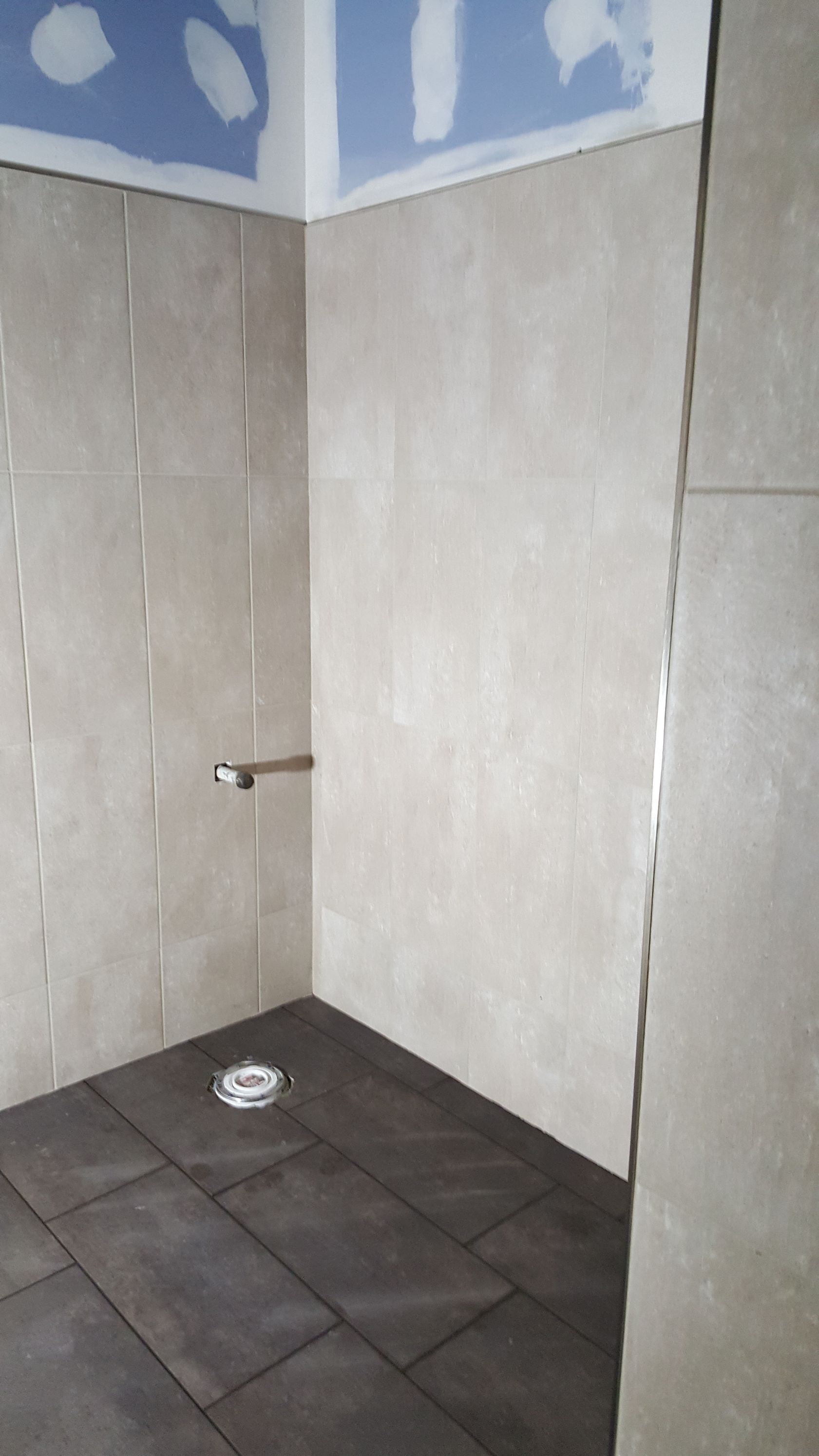 Shower stall with beige tile walls and dark brown tile floor.
