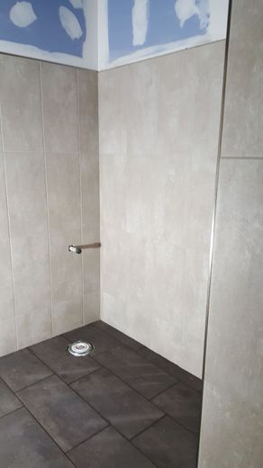 Shower stall under construction; tan tile walls, dark tile floor.
