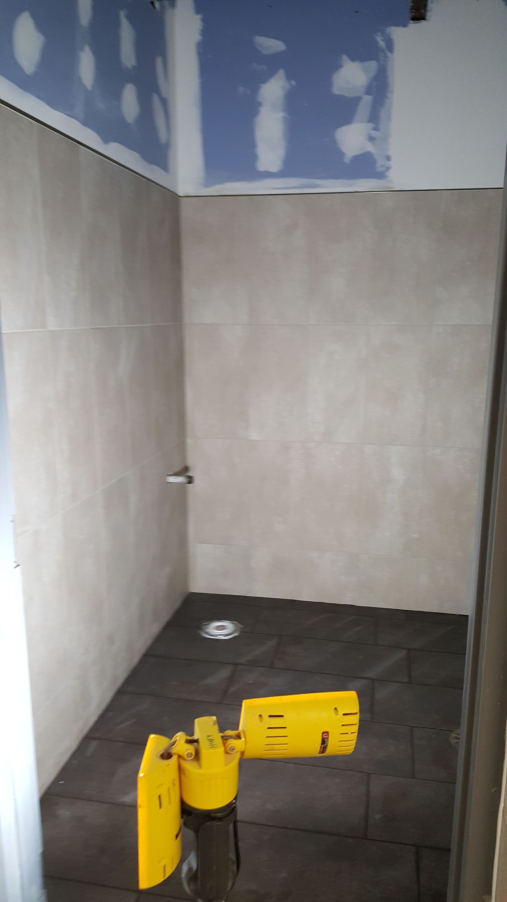 Shower under construction, beige tile walls, dark floor, yellow construction light.