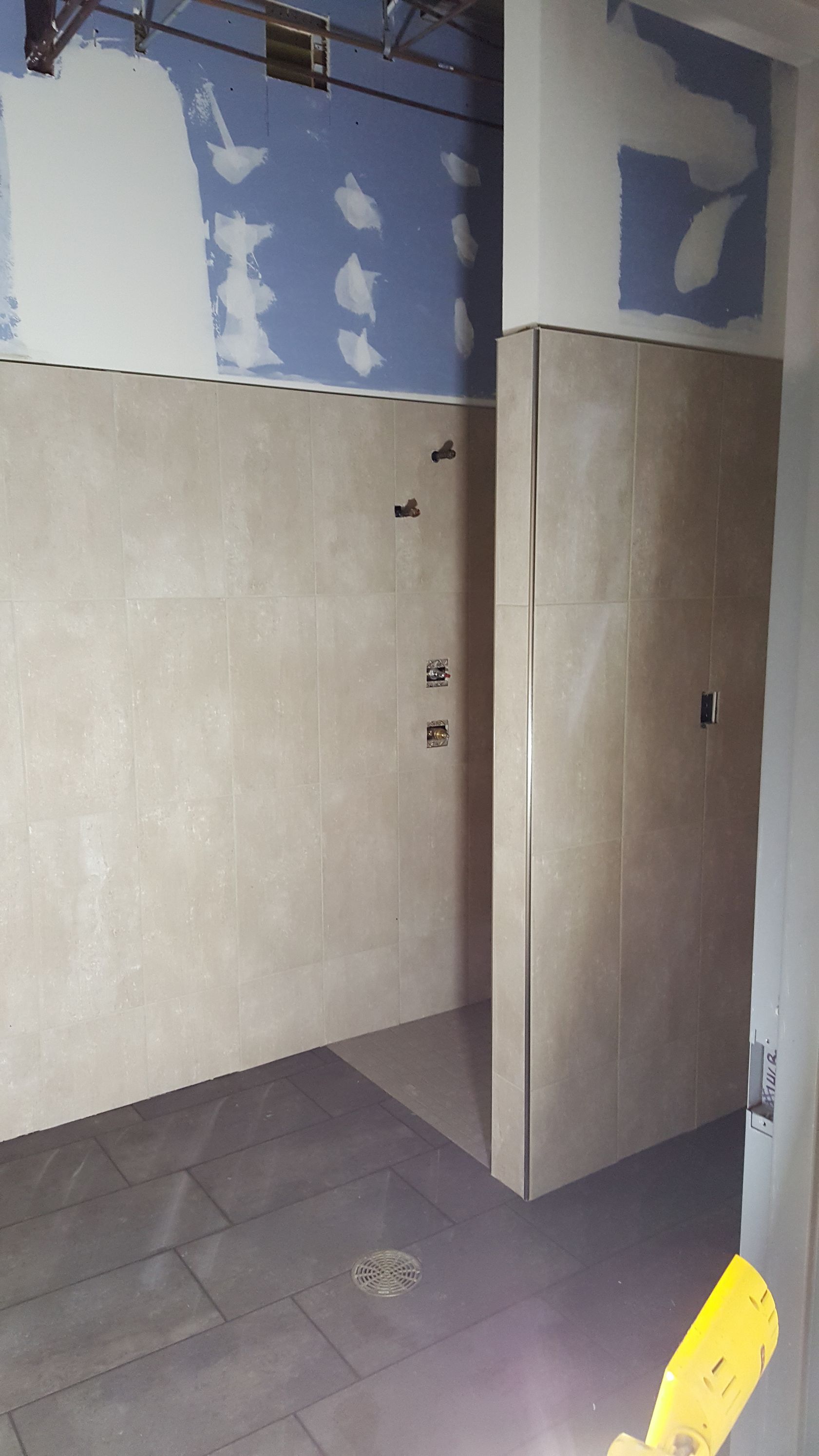 Bathroom under construction with beige tile walls, dark floor, and blue drywall.