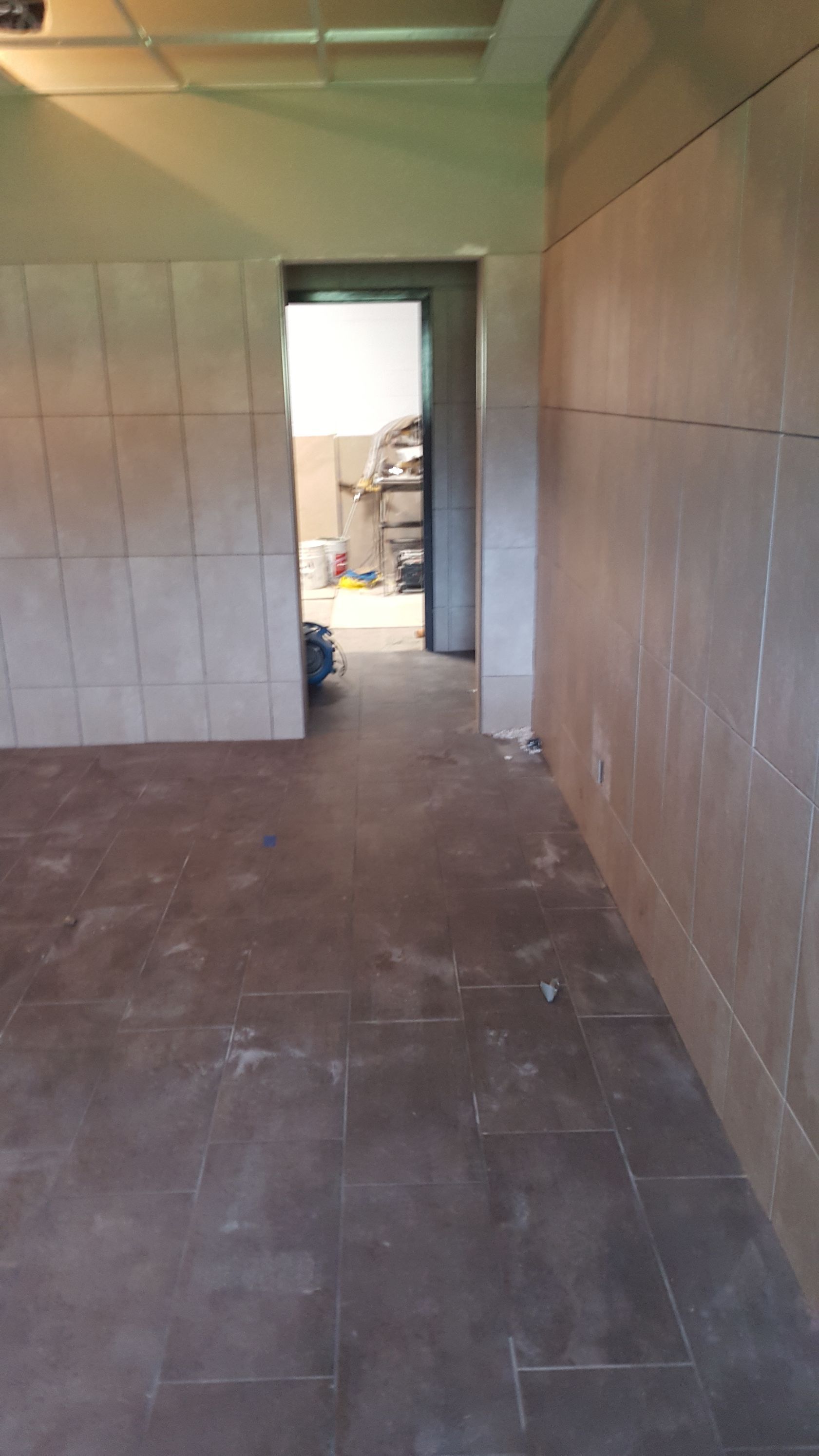 Empty room with tiled walls and floor; doorway leads to another area.