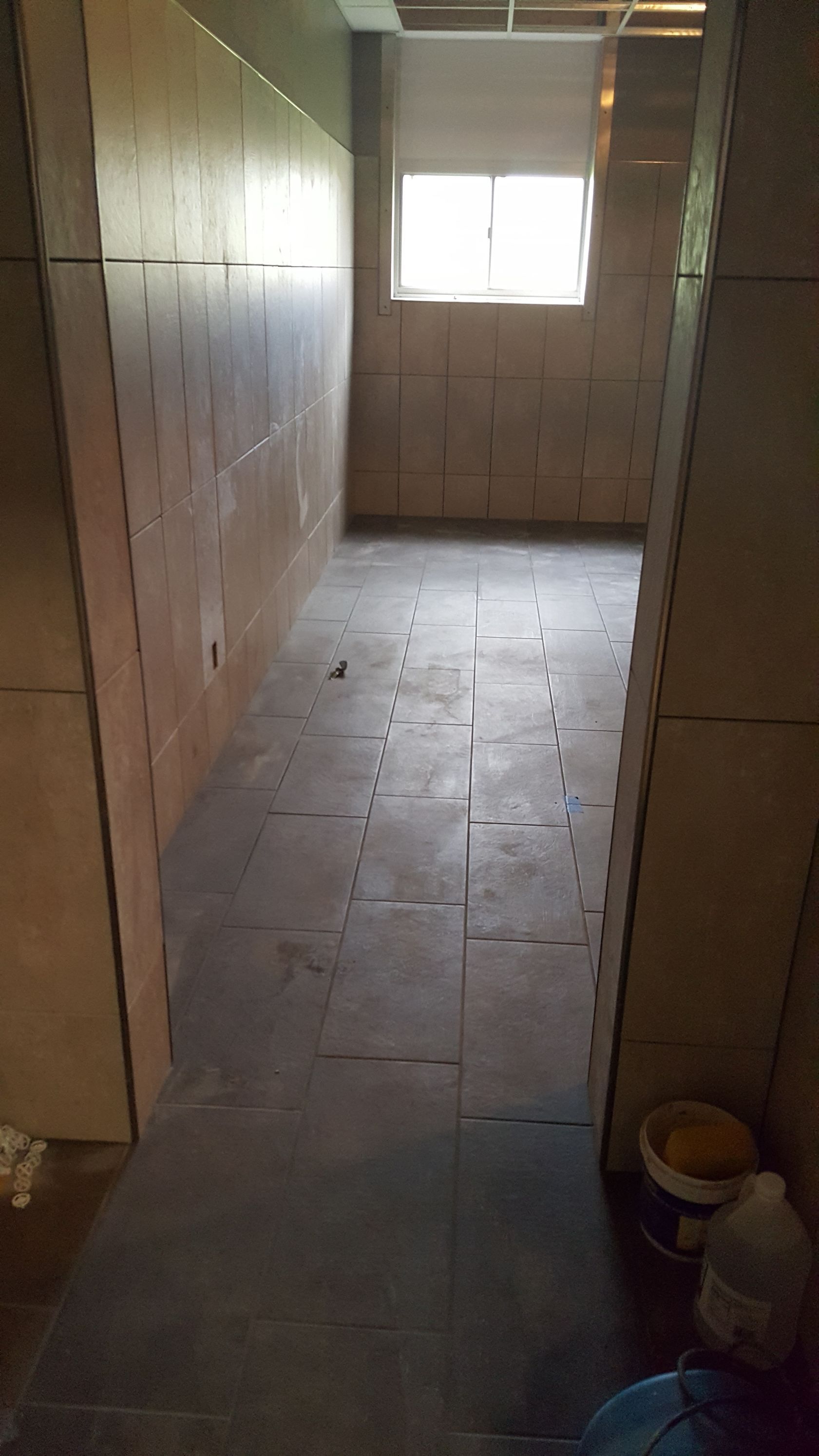 Empty hallway with dark tiled floor, light wood walls, and a window at the end.