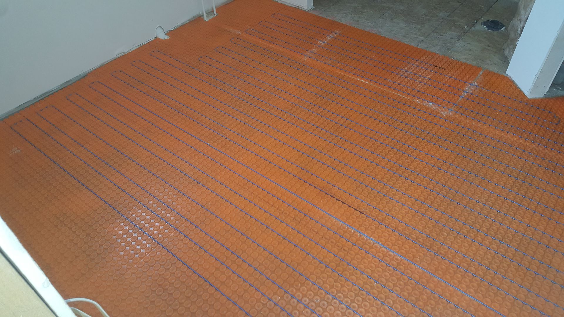 Orange radiant floor heating mat laid on a cement floor, ready for tiling.