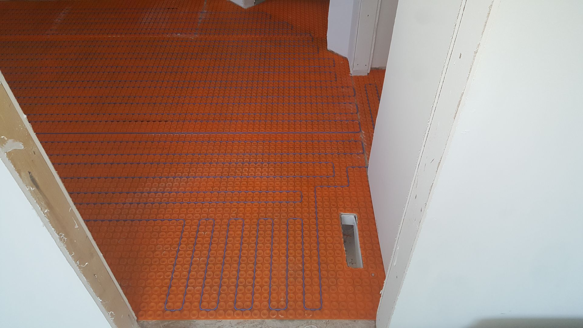 Orange floor underlayment installed in a doorway between white walls, ready for tiling.