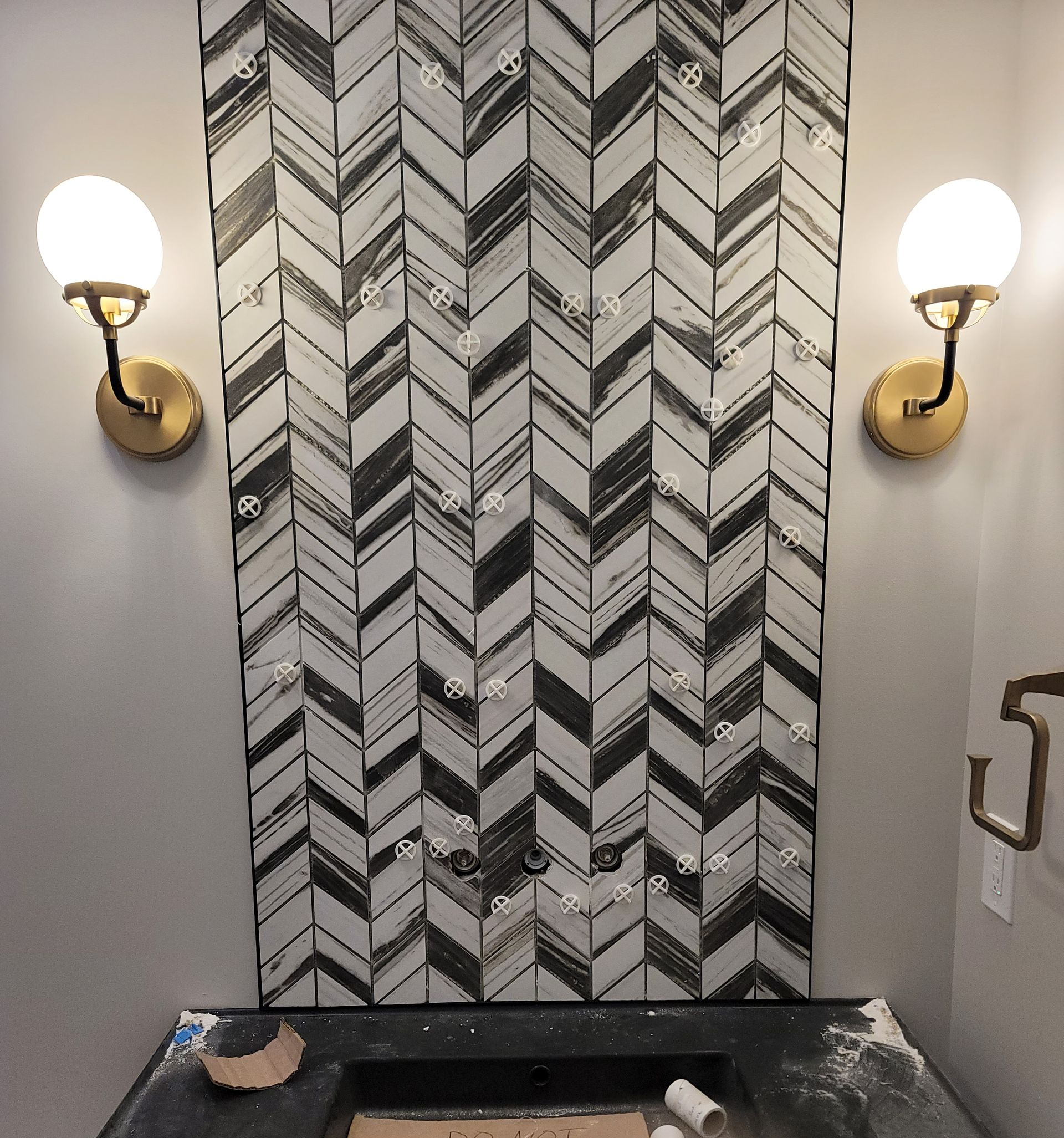 Bathroom wall with patterned black and white tile, globe sconces on the sides, and a black sink.