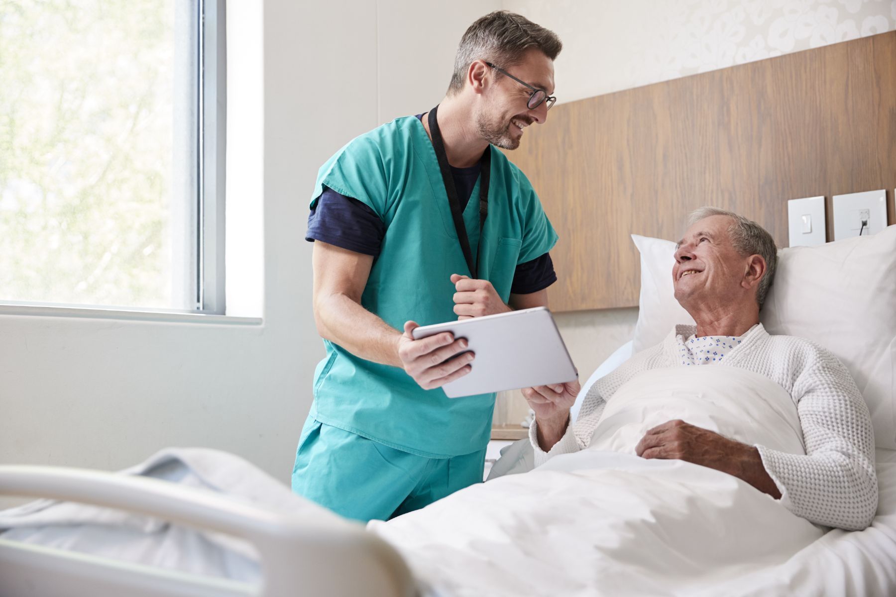 male surgeon talking to elderly male patient in hospital bed