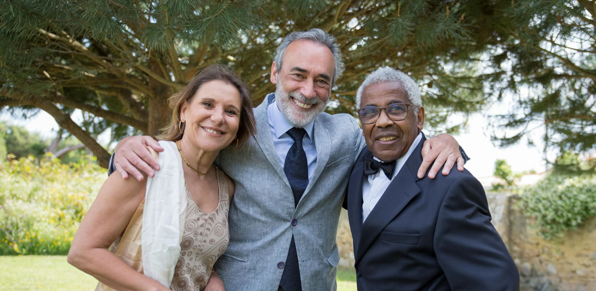 A man and two women are posing for a picture in front of a tree.