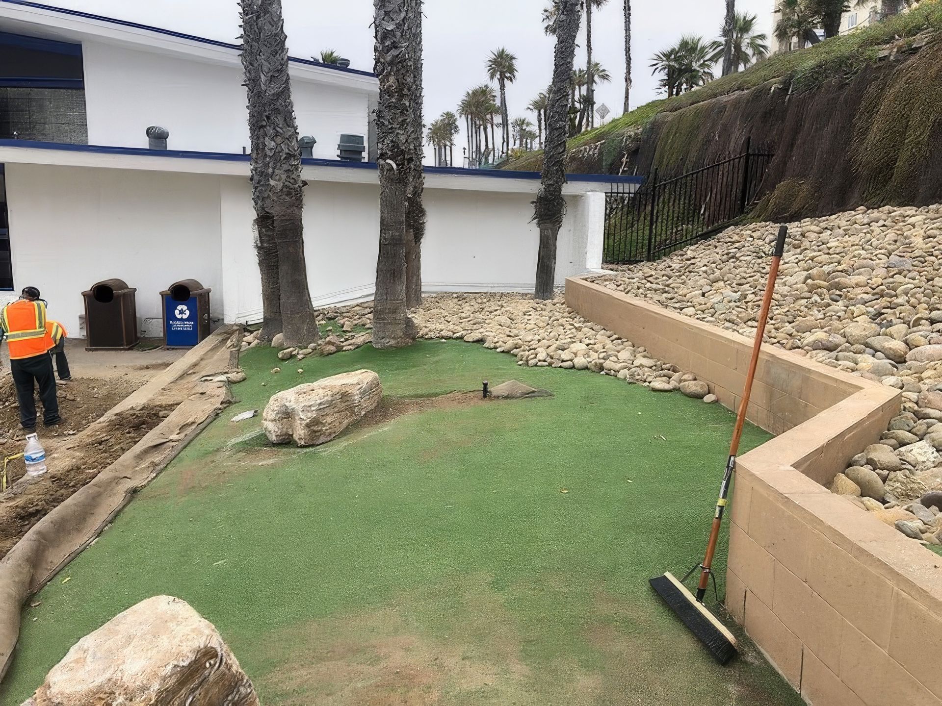 A man in an orange vest is standing next to a broom on a golf course.