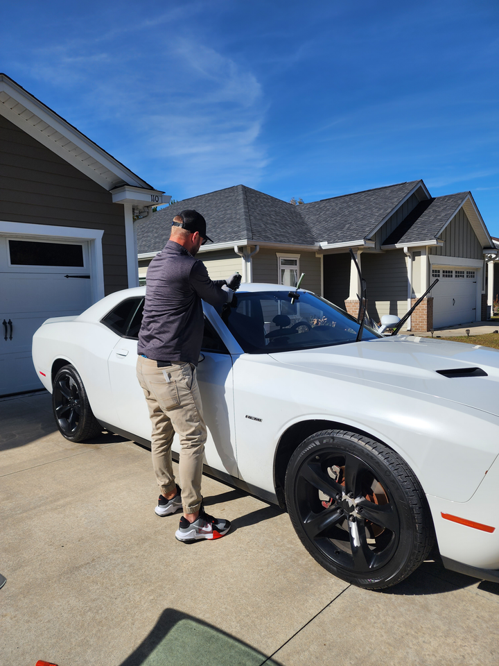 Mechanic applying sealant to a windshield in a garage. Blue car in background.