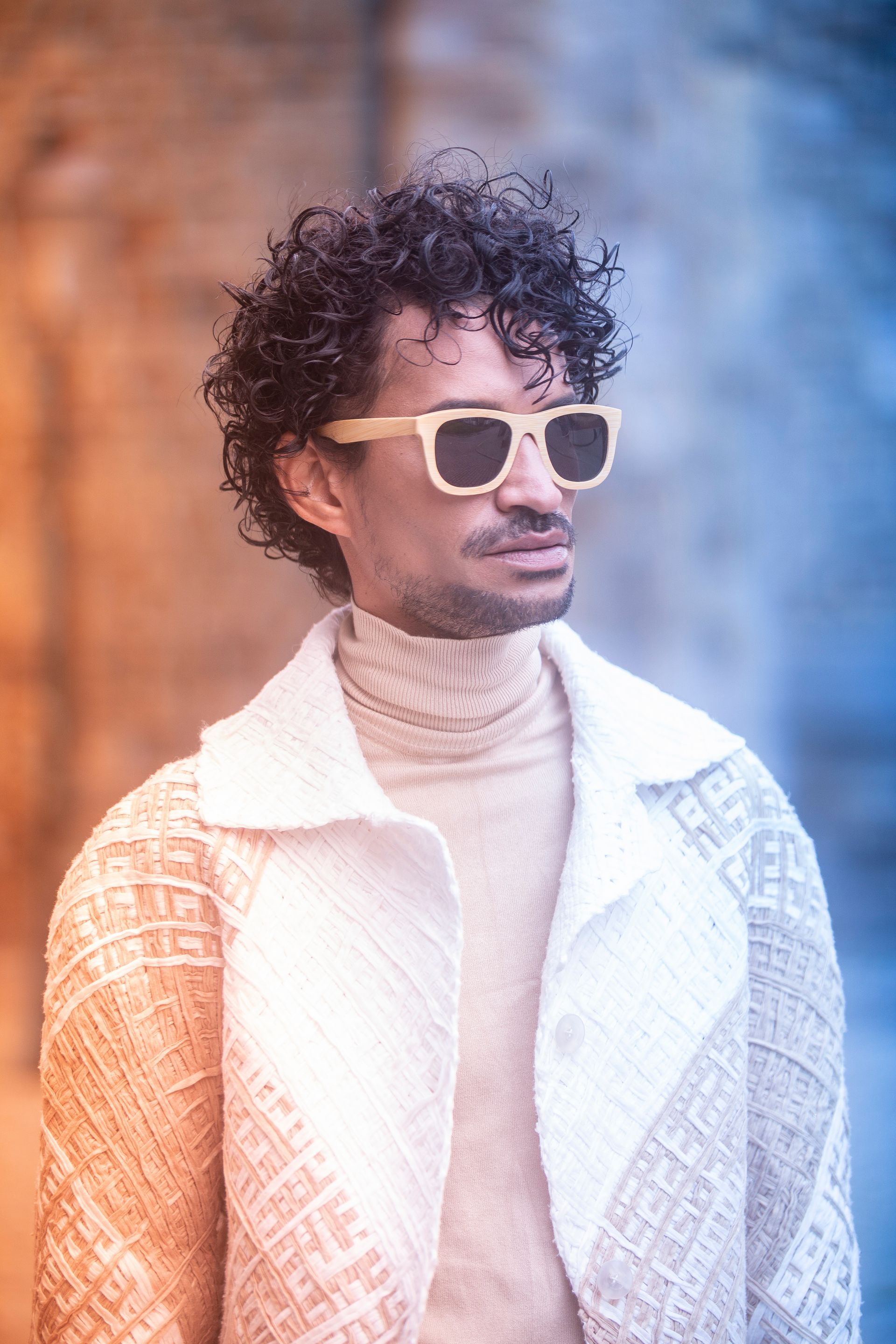 Um homem usando óculos escuros e um suéter está parado em frente a um prédio.