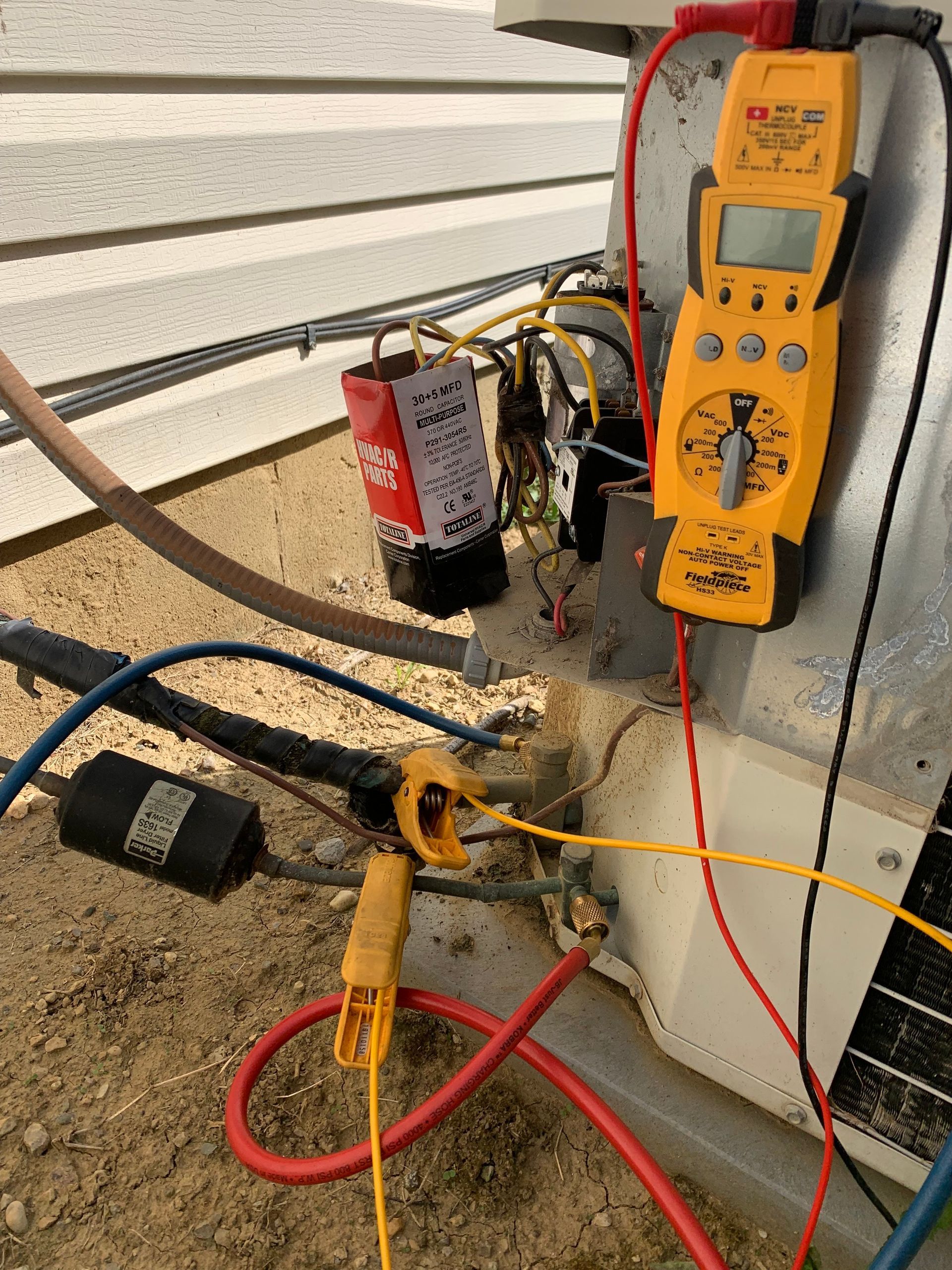 HVAC technician using a multimeter to test electrical components on an outdoor air conditioning unit.