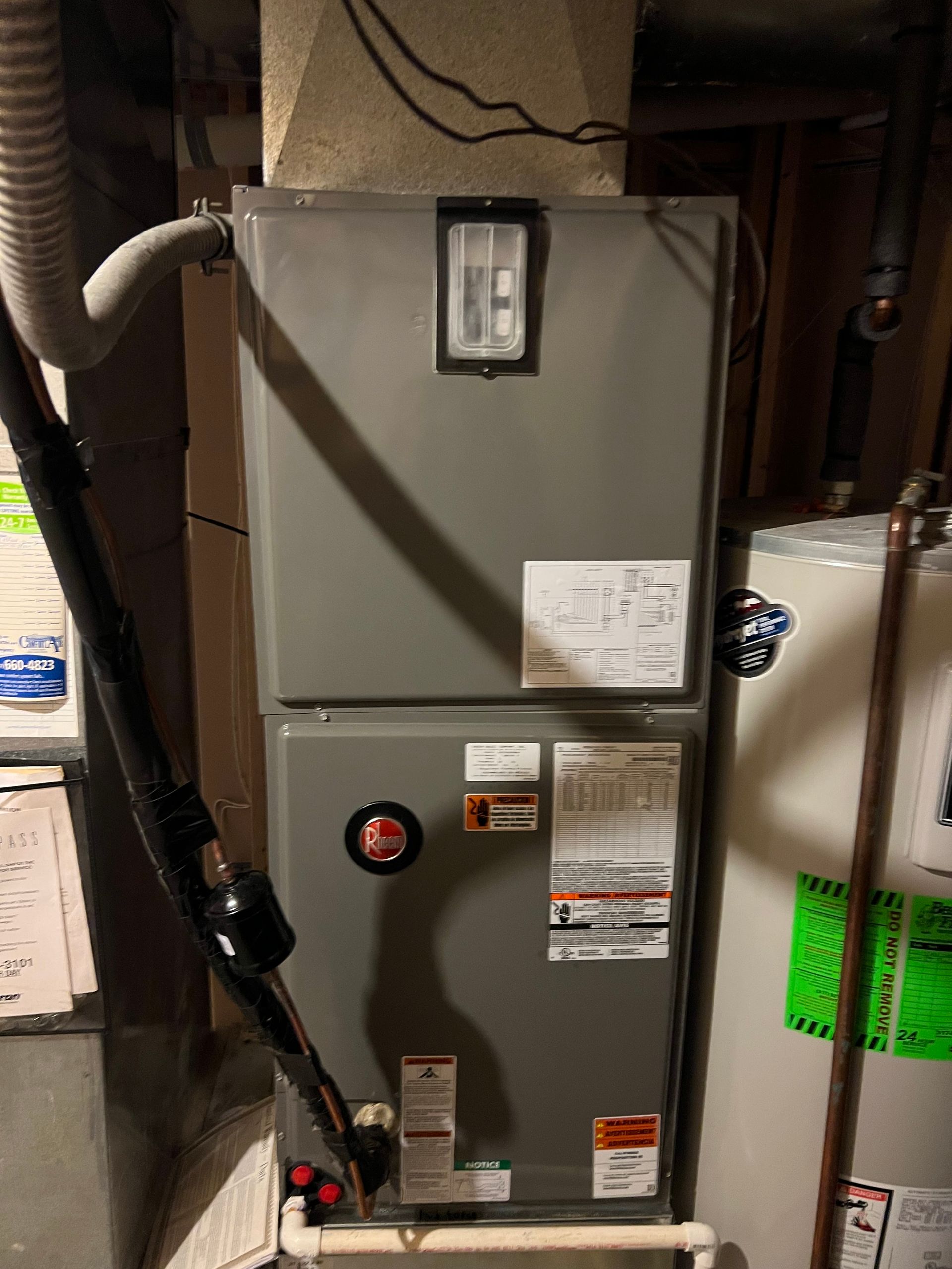 Gray furnace and water heater in a basement setting with ductwork and pipes visible.