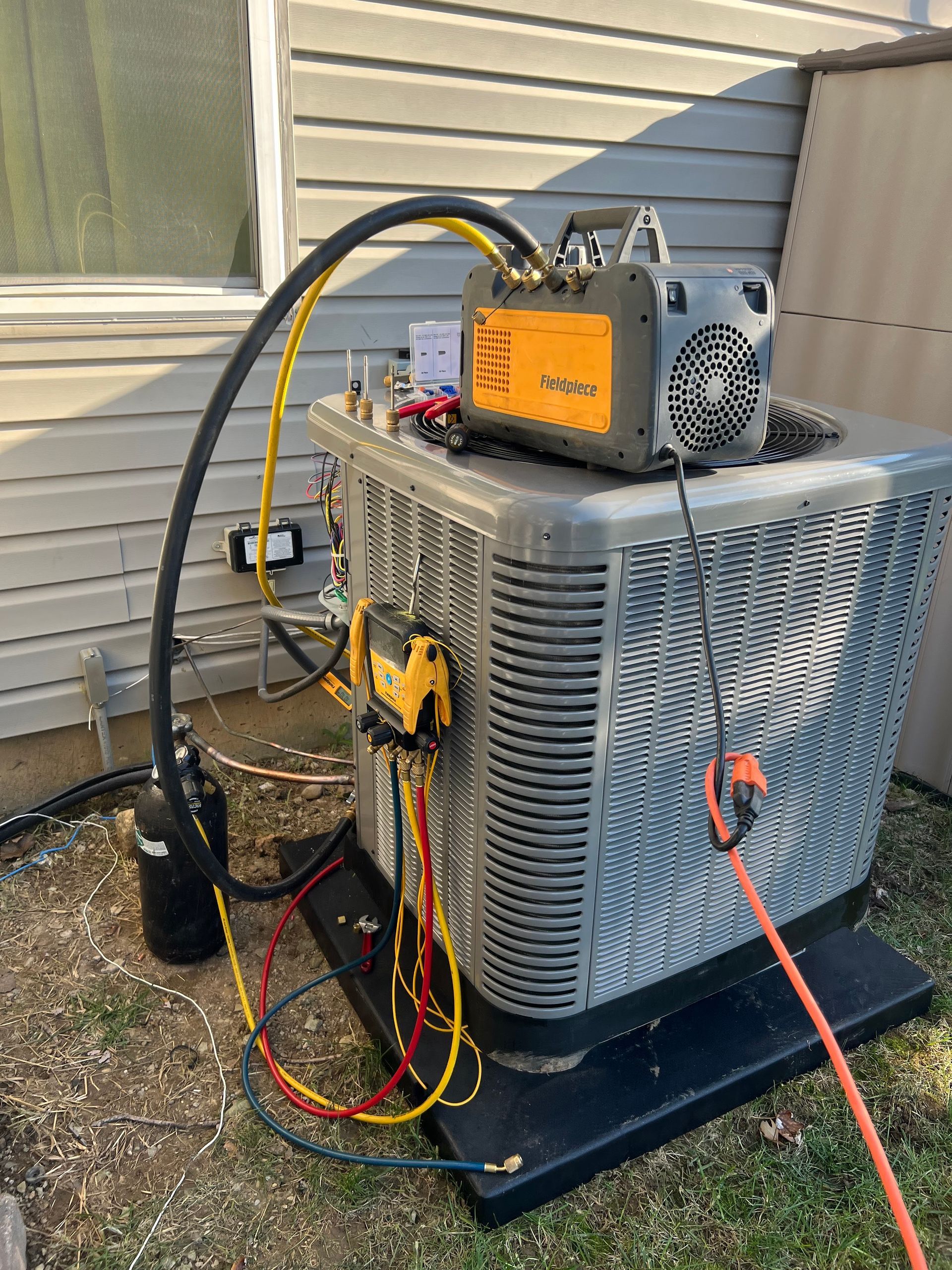 HVAC technician servicing an air conditioning unit. Black hose and yellow/red gauges attached.