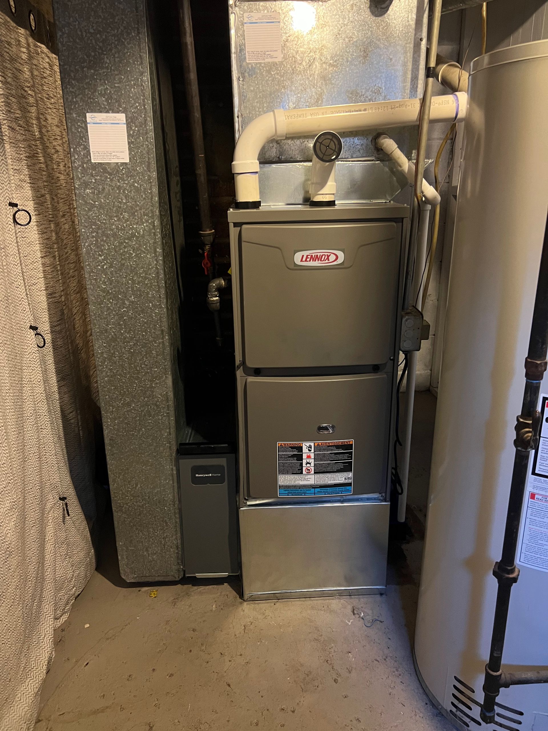 Furnace and water heater in a utility room. Gray metal appliances and ductwork. Beige walls and floor.