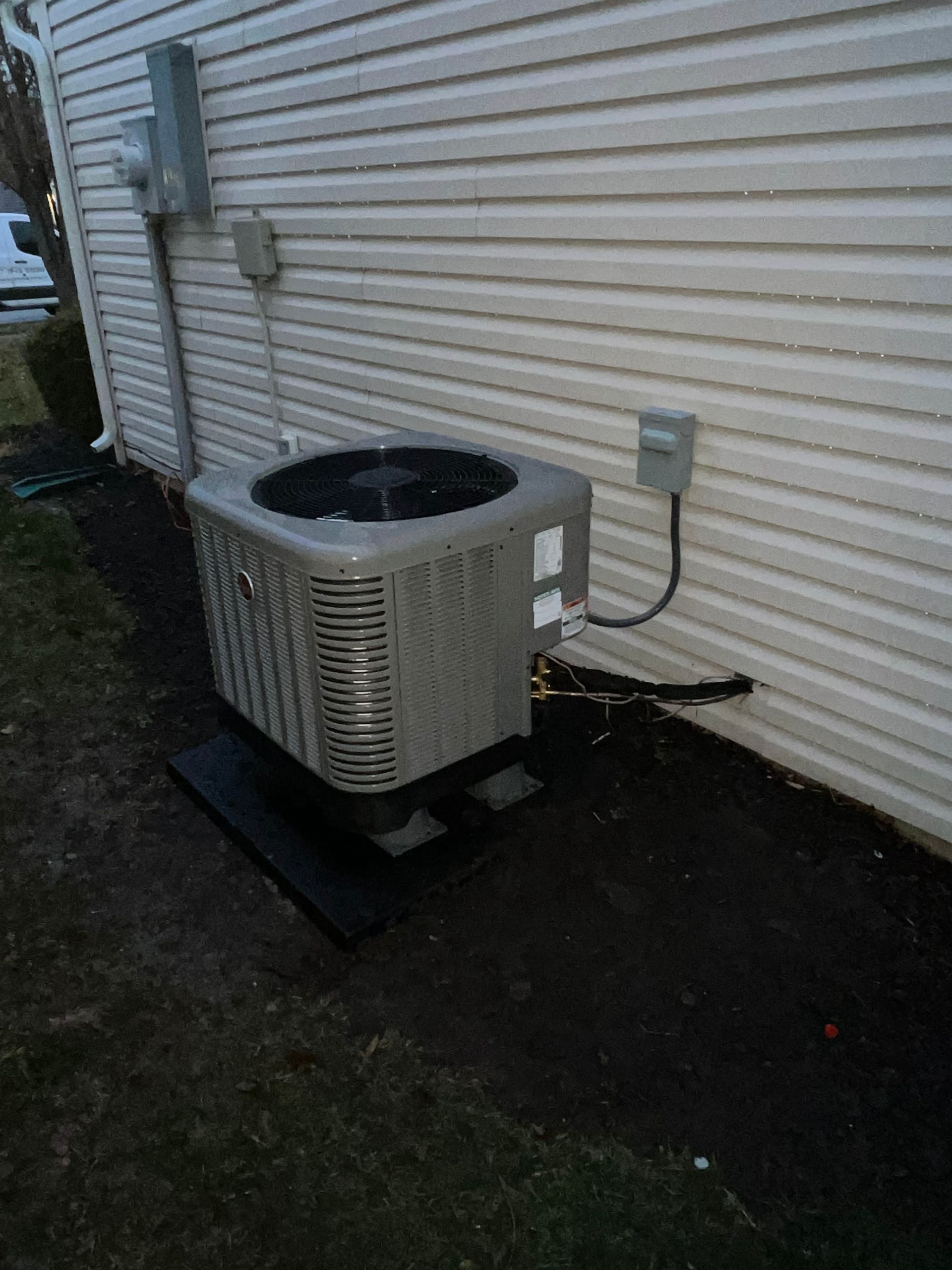 Air conditioning unit outside a house, with electrical connections on the siding.