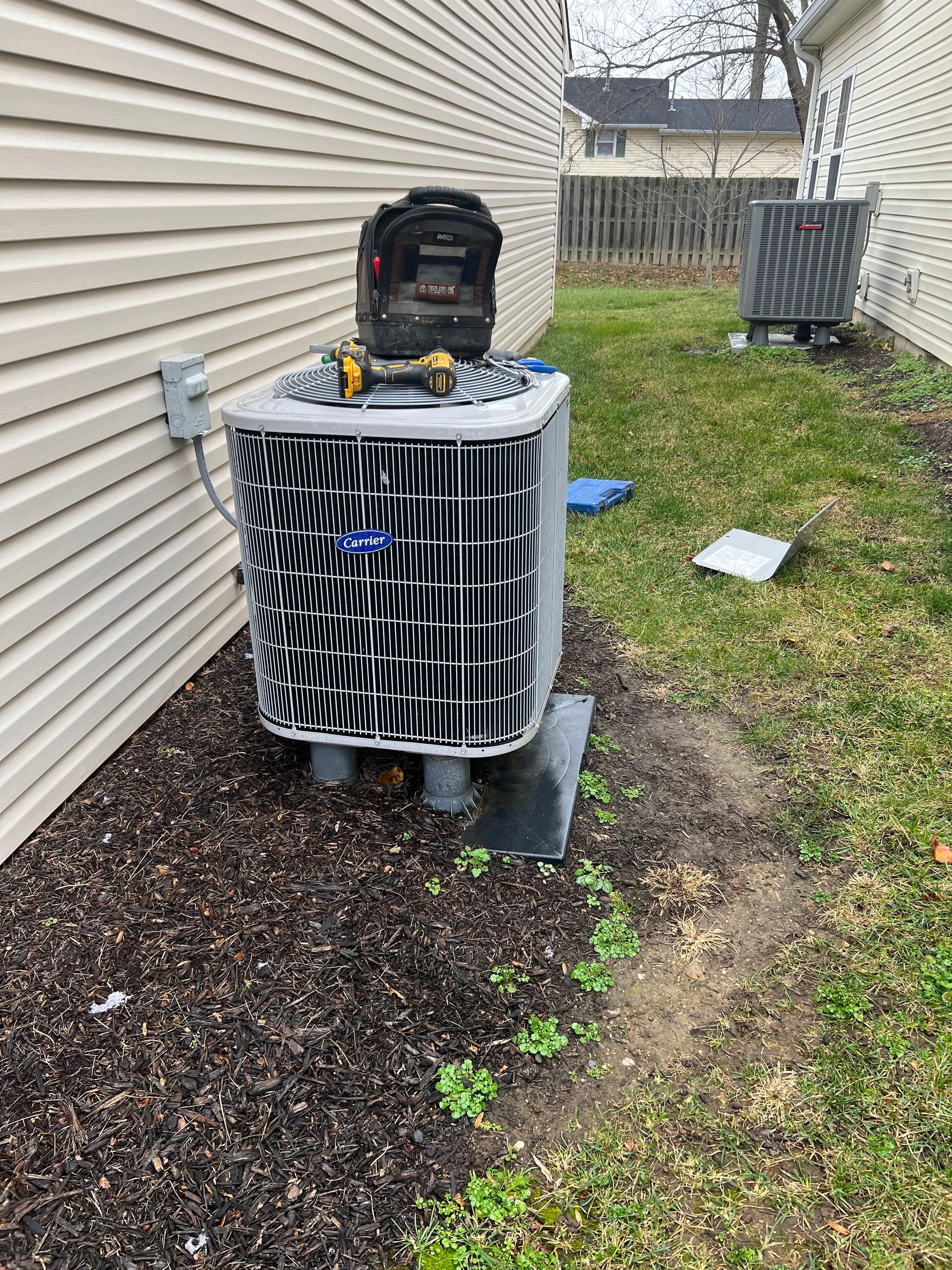 HVAC unit outside a building with brown mulch and grass. Tools sit on top.