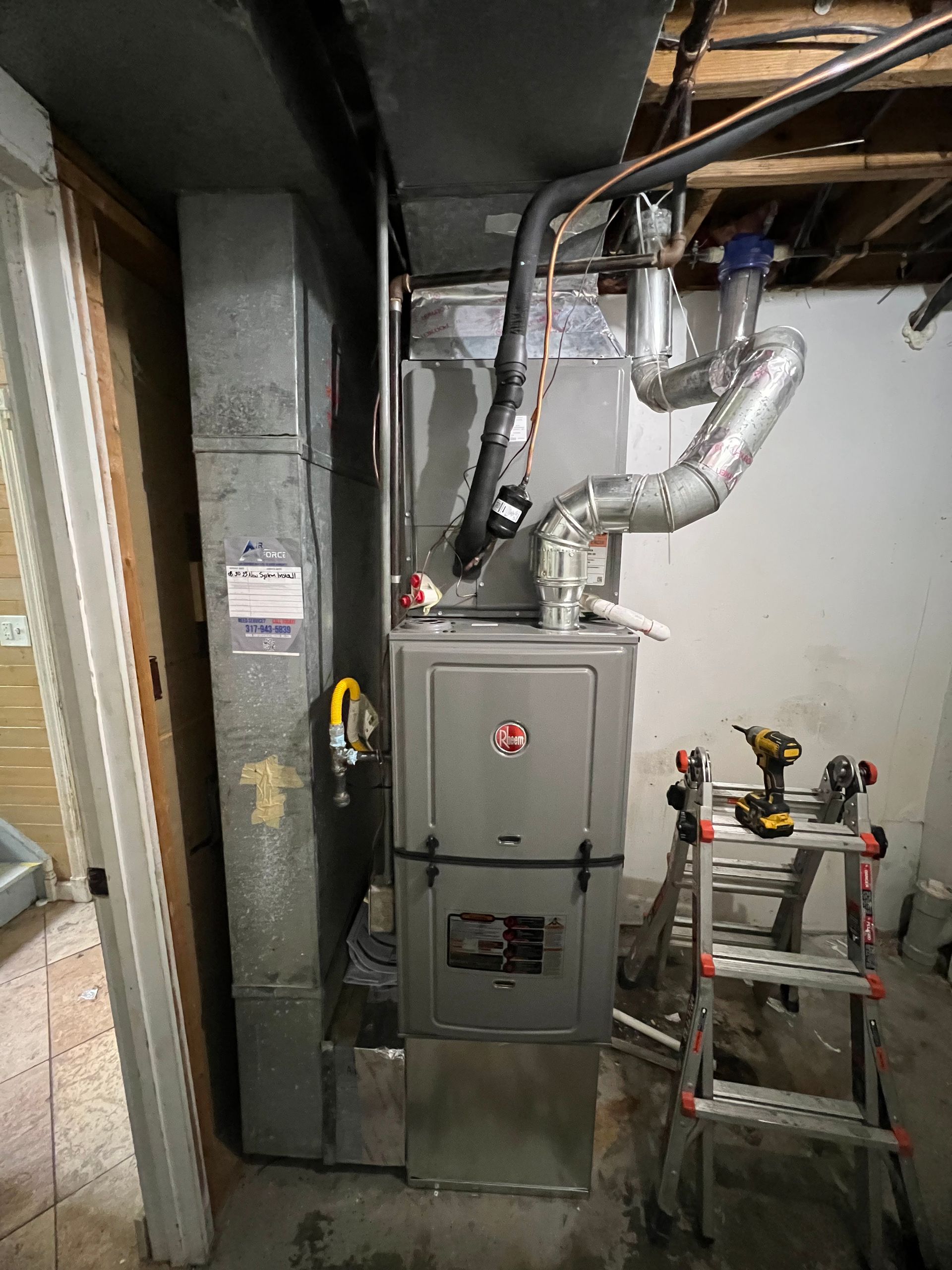 Furnace and ductwork installation in a basement. Silver metal, gray, and black components. A small ladder is present.