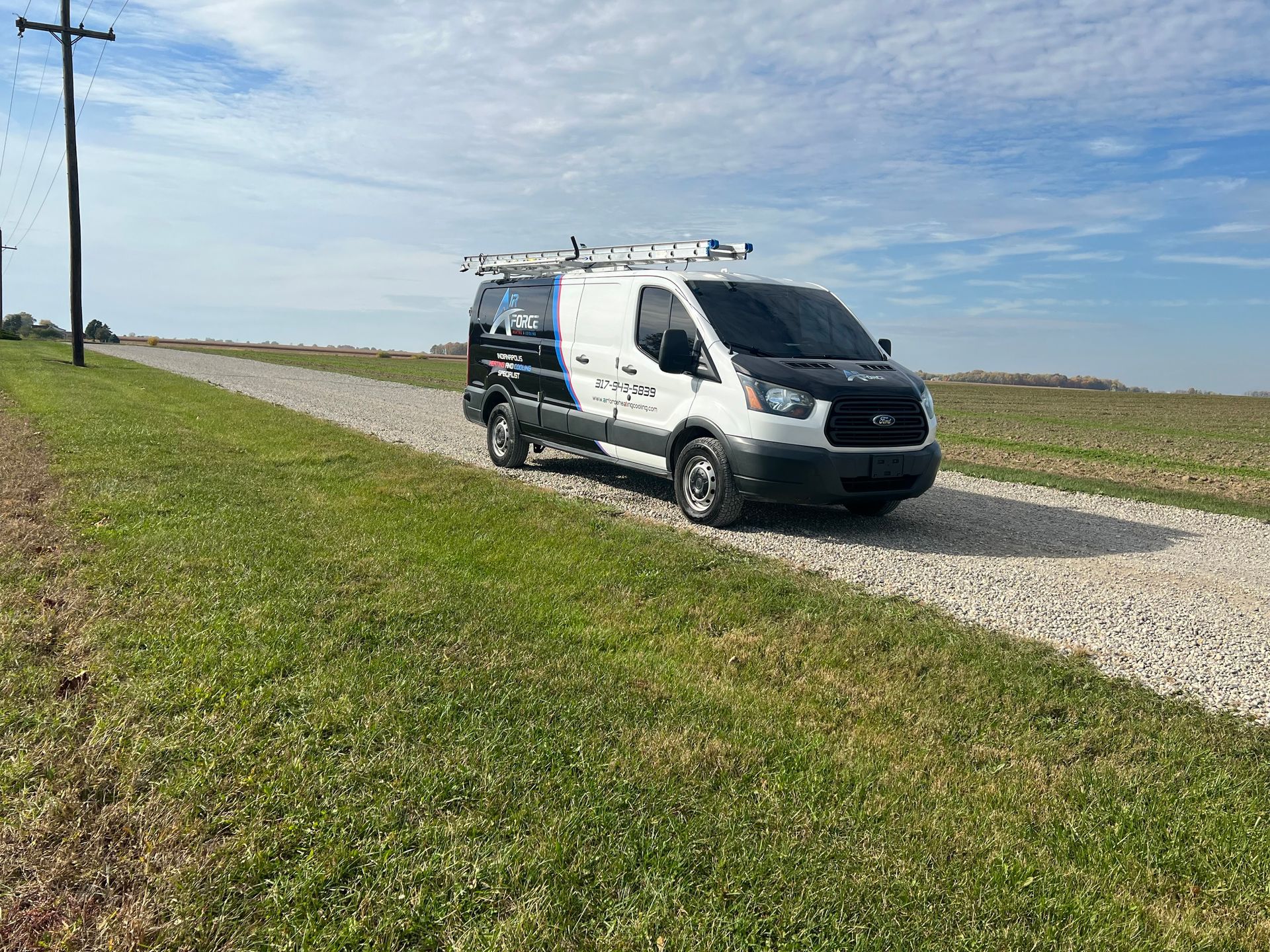 White service van on a gravel road, roof rack, driving across a grassy area under a blue sky.