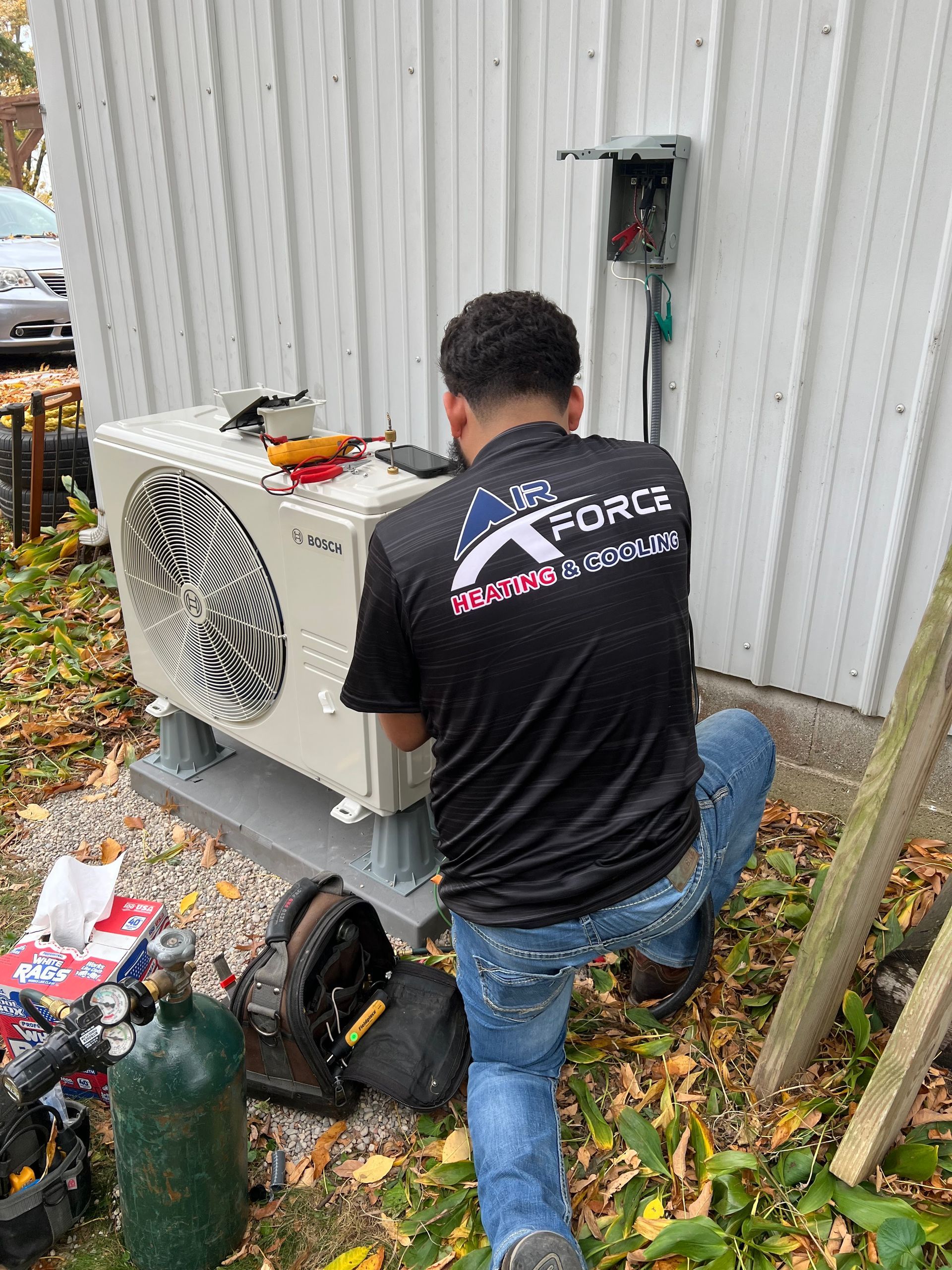 HVAC technician installing an outdoor air conditioning unit next to a white building.