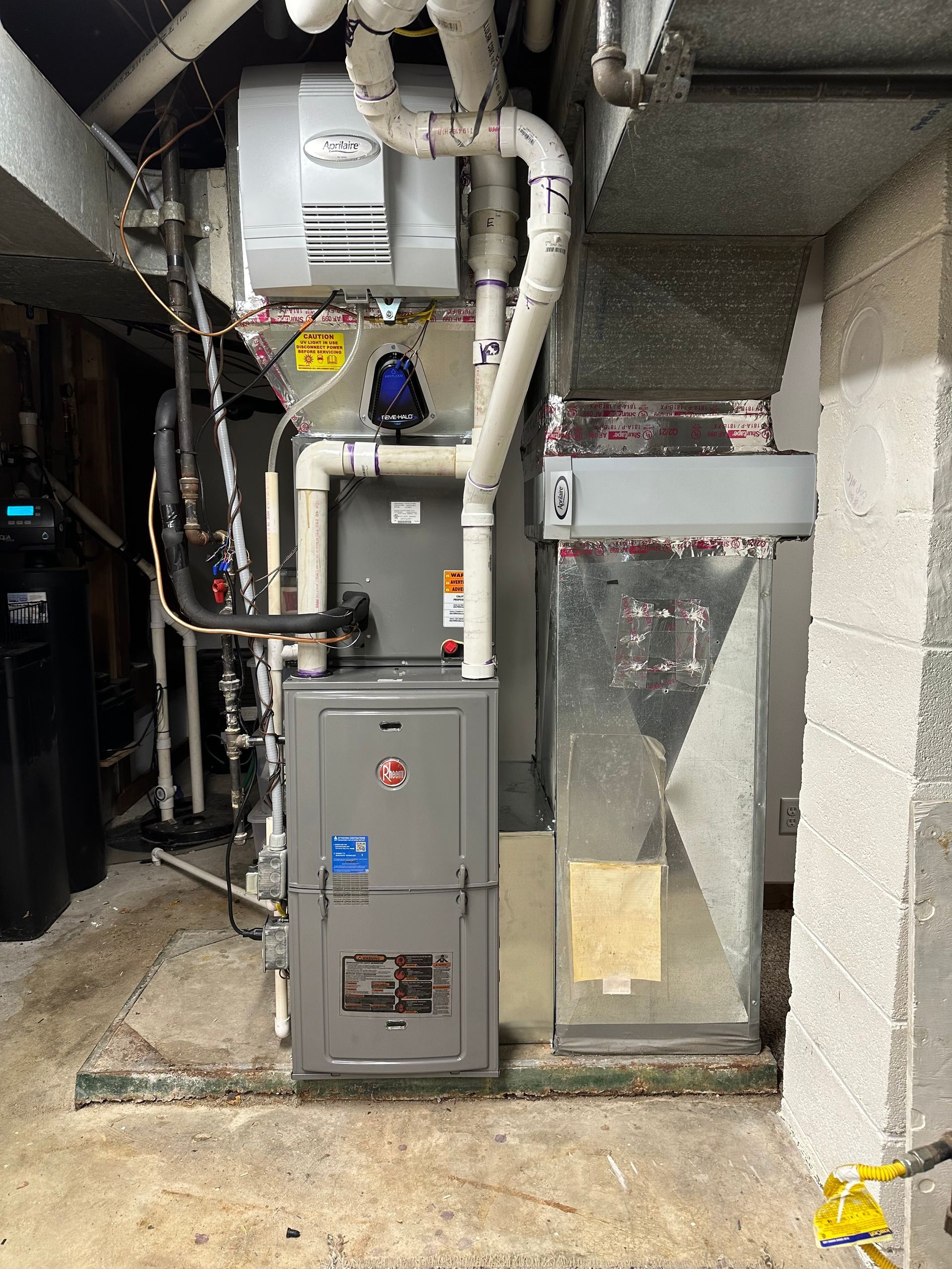 A furnace and attached ductwork in a basement setting. Pipes and a humidifier are present.