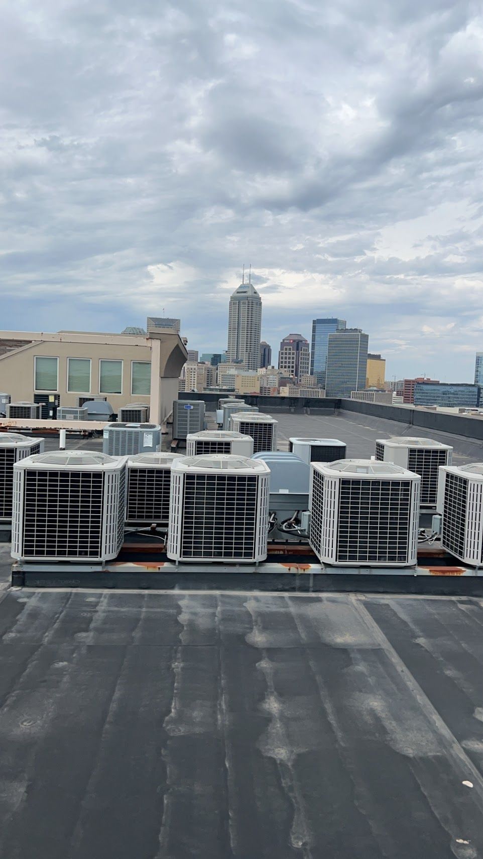 Rooftop view of air conditioning units, with a city skyline in the background under a cloudy sky.