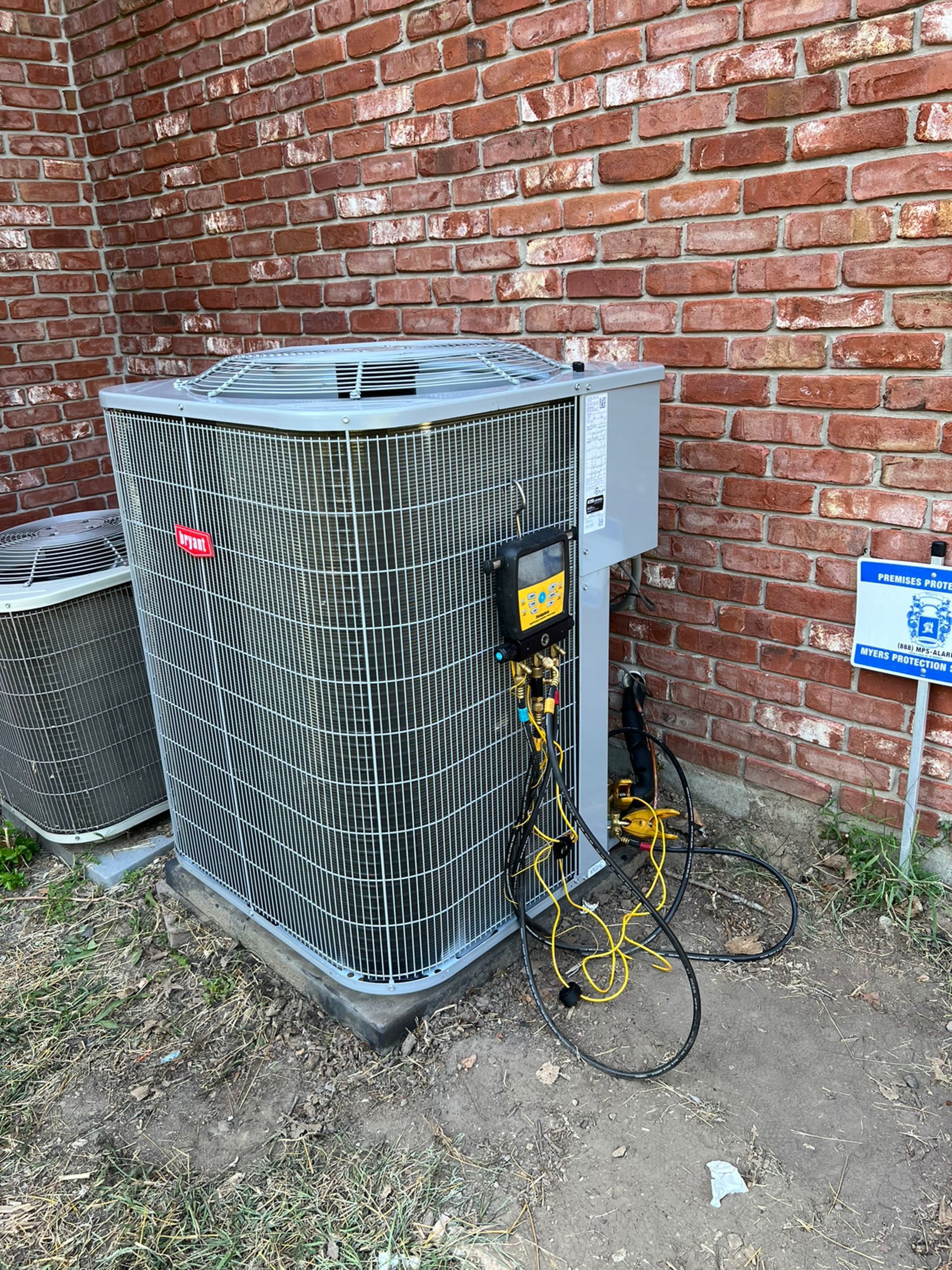 Air conditioning unit next to a brick wall with yellow gauges attached.