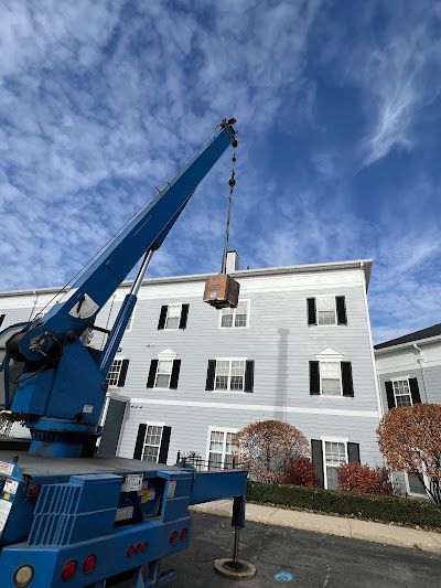 A blue crane lifting a brown box towards a light blue apartment building under a cloudy sky.