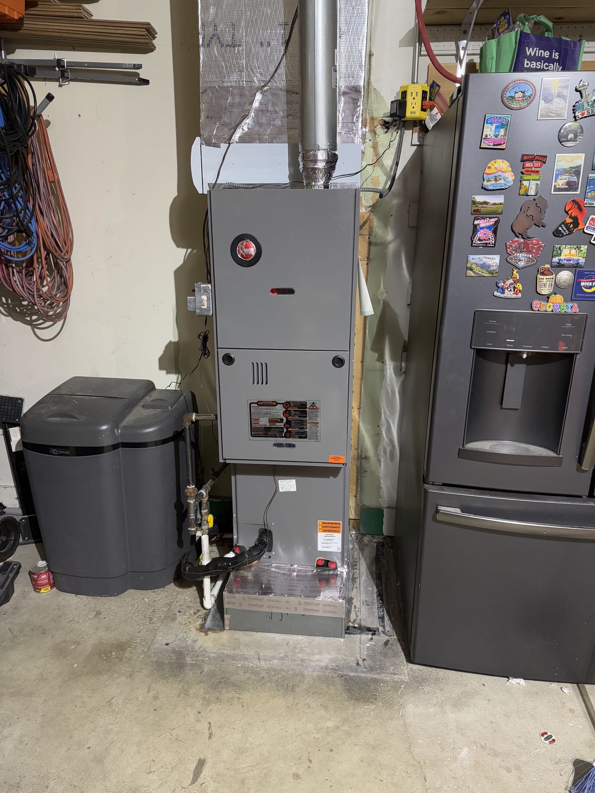 Furnace unit in a garage next to a refrigerator and trash can.