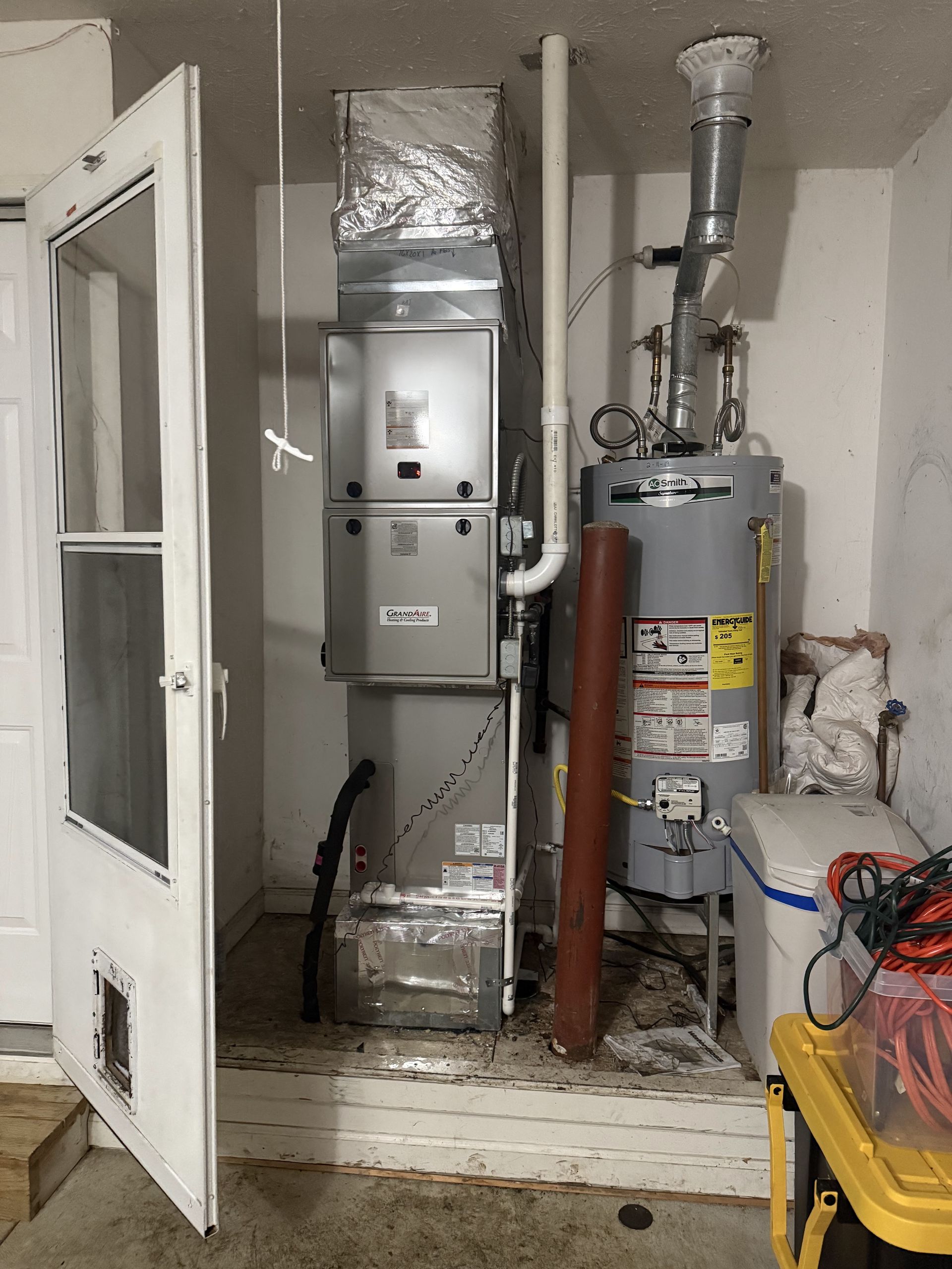 HVAC system and water heater in a utility room next to a white door.