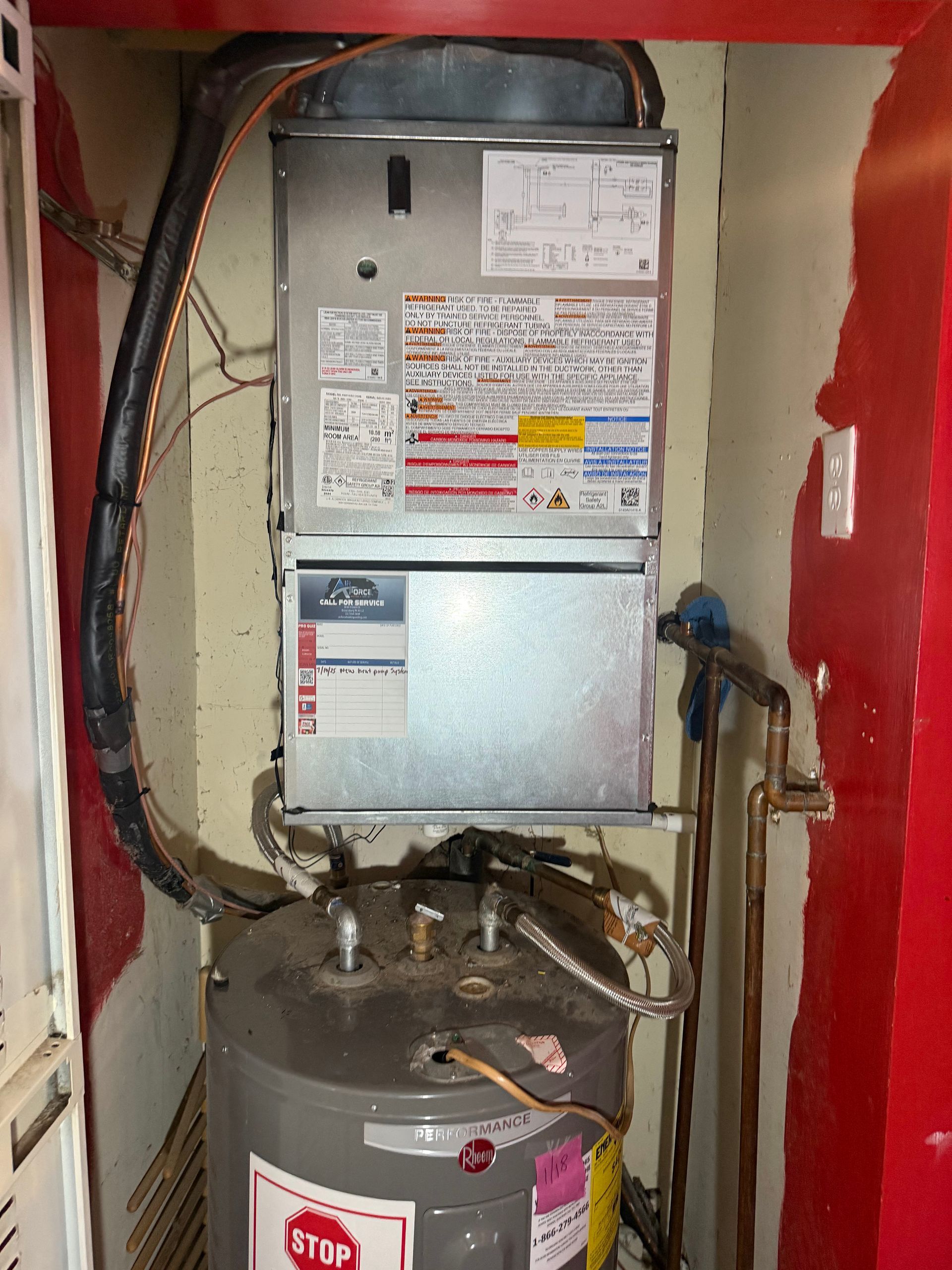 A gas furnace and water heater are mounted vertically in a utility closet with red walls.