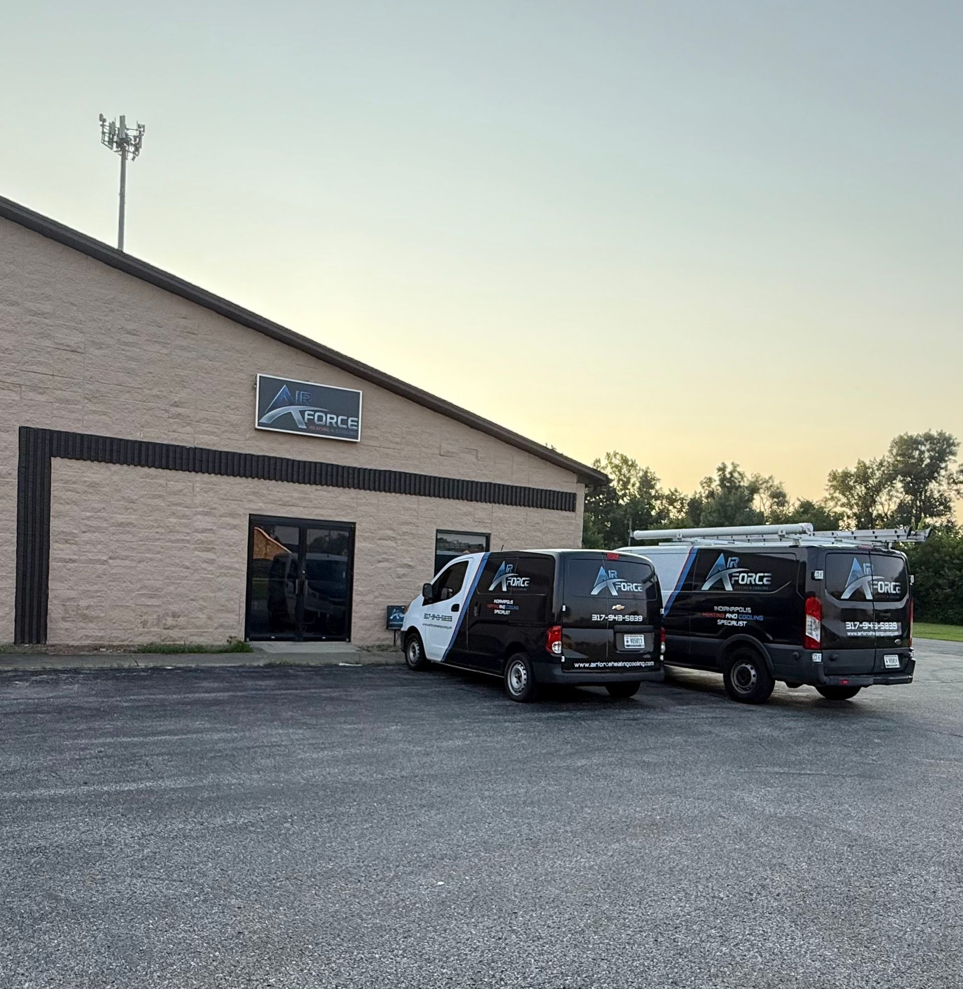 Two black and white vans parked in front of a brick building with a sign; dusk sky.
