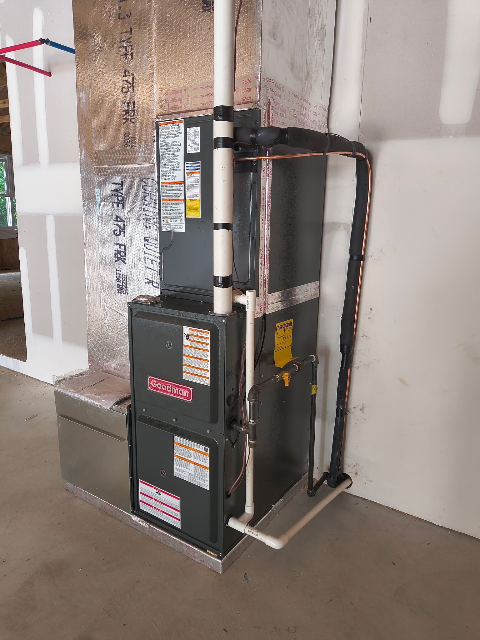 HVAC unit in unfinished room. Ductwork, piping, and labels are visible on the metal structure.