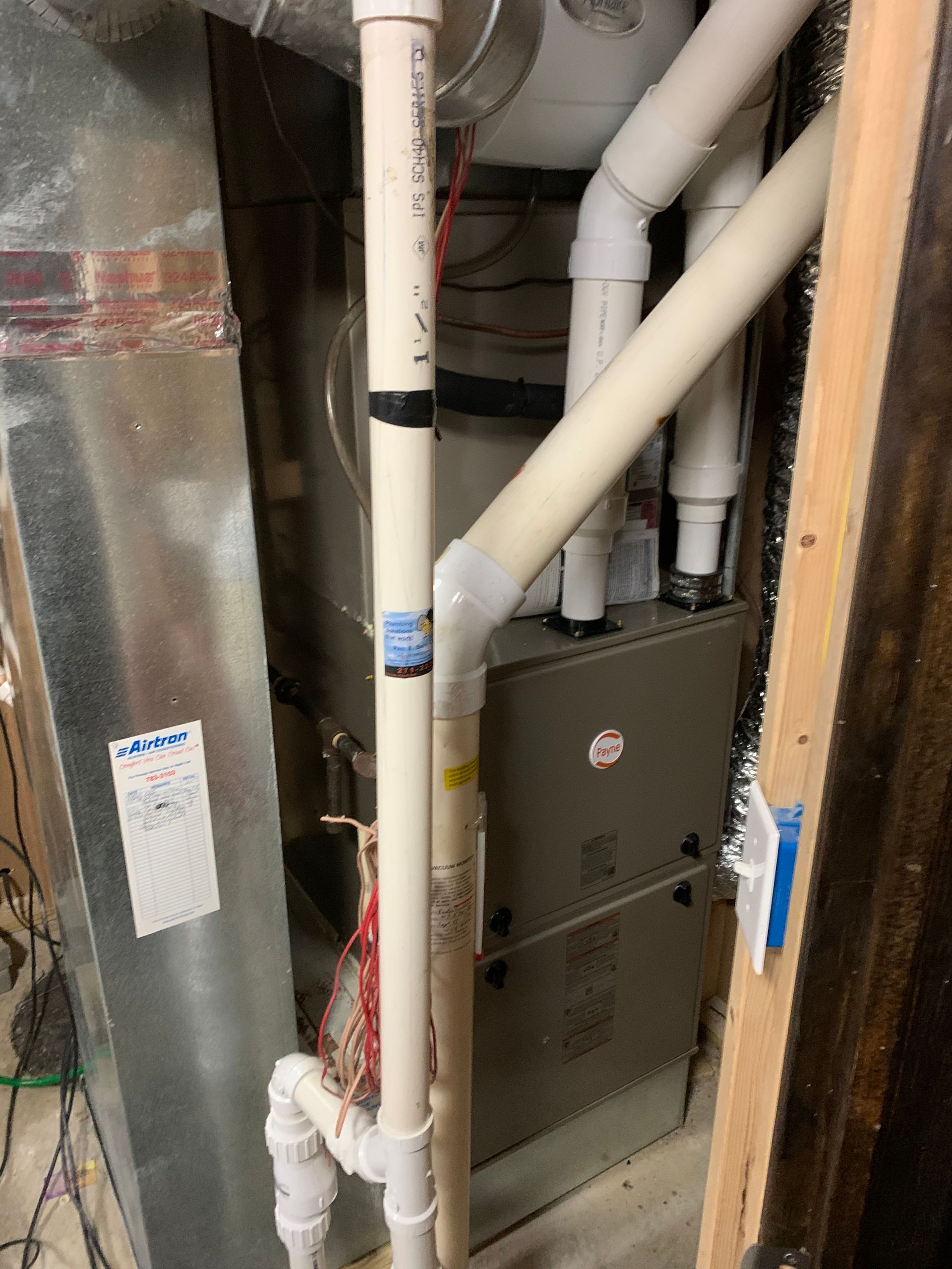 Furnace with white PVC pipes for exhaust, metal ductwork, and electrical wiring in a basement.