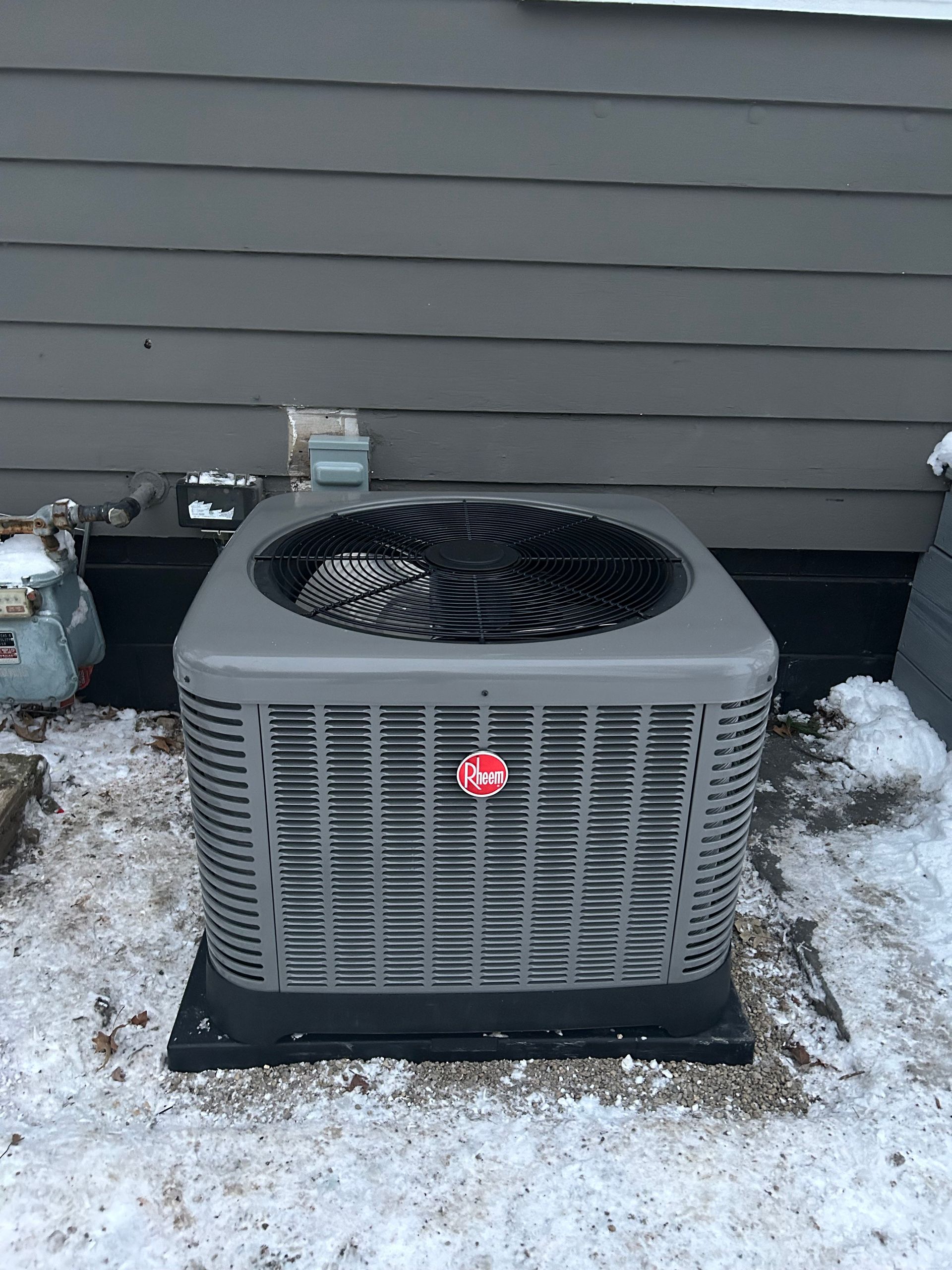 Gray Rheem air conditioning unit on a snow-covered rooftop.
