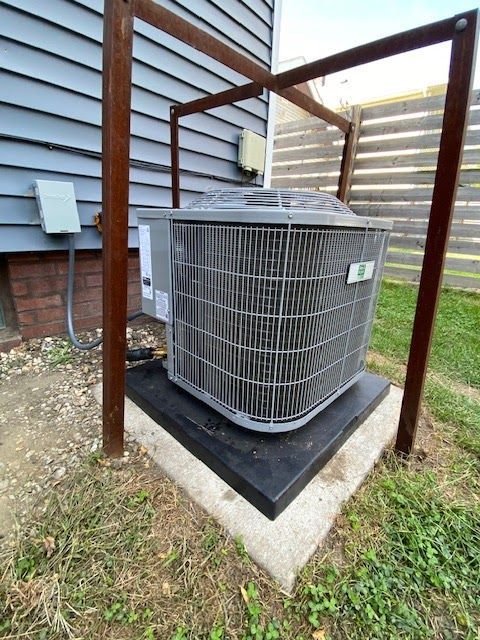 Air conditioner unit outside a house, protected by a metal frame and sitting on a concrete pad.