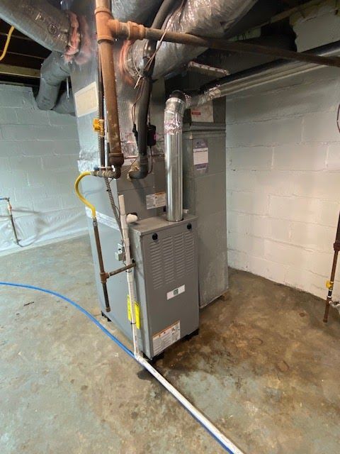 Furnace and air conditioning unit in a basement setting with ductwork and piping.