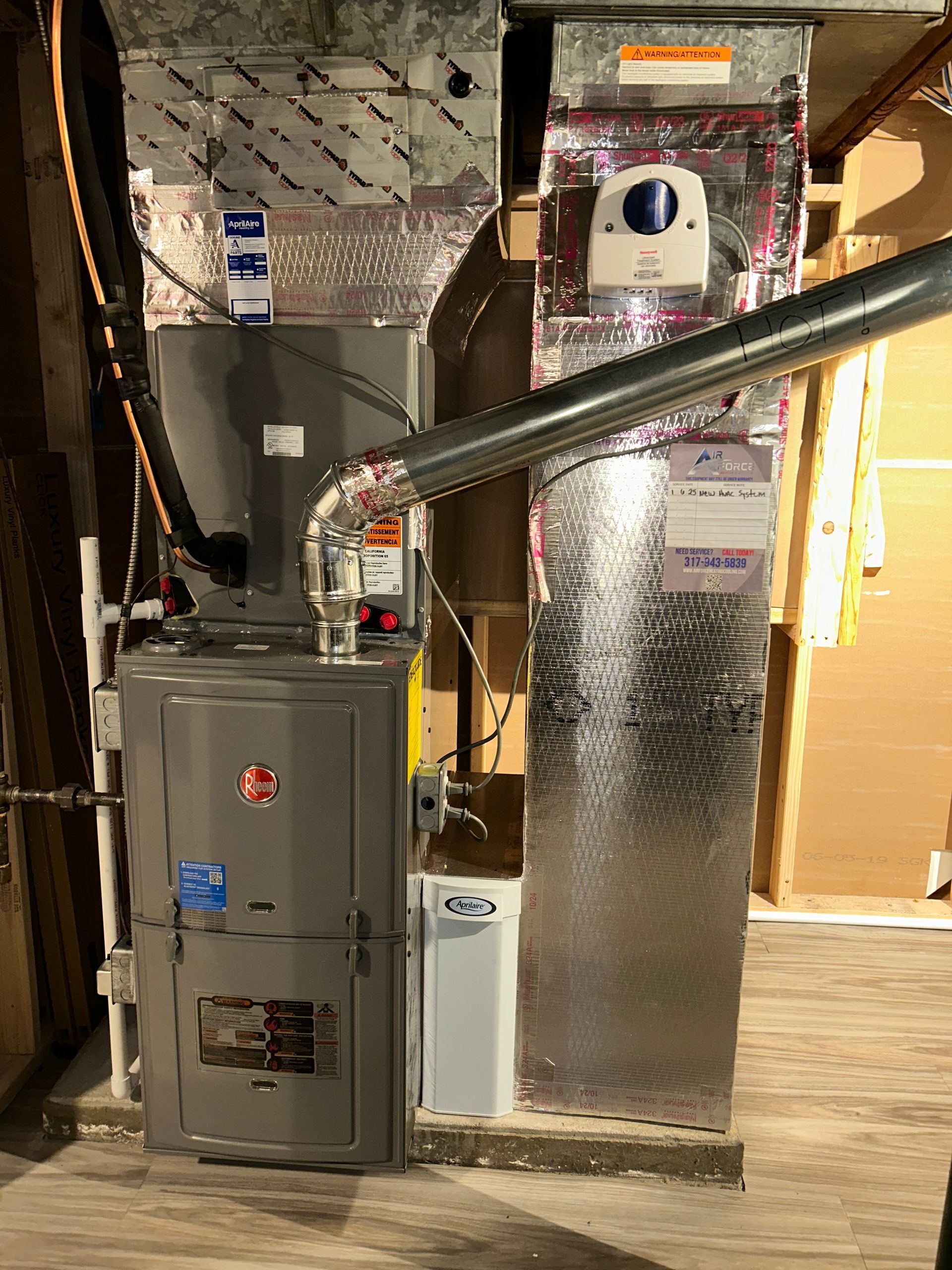 Furnace and ductwork in a utility room. Gray metal furnace with silver insulated ducts. White humidifier.