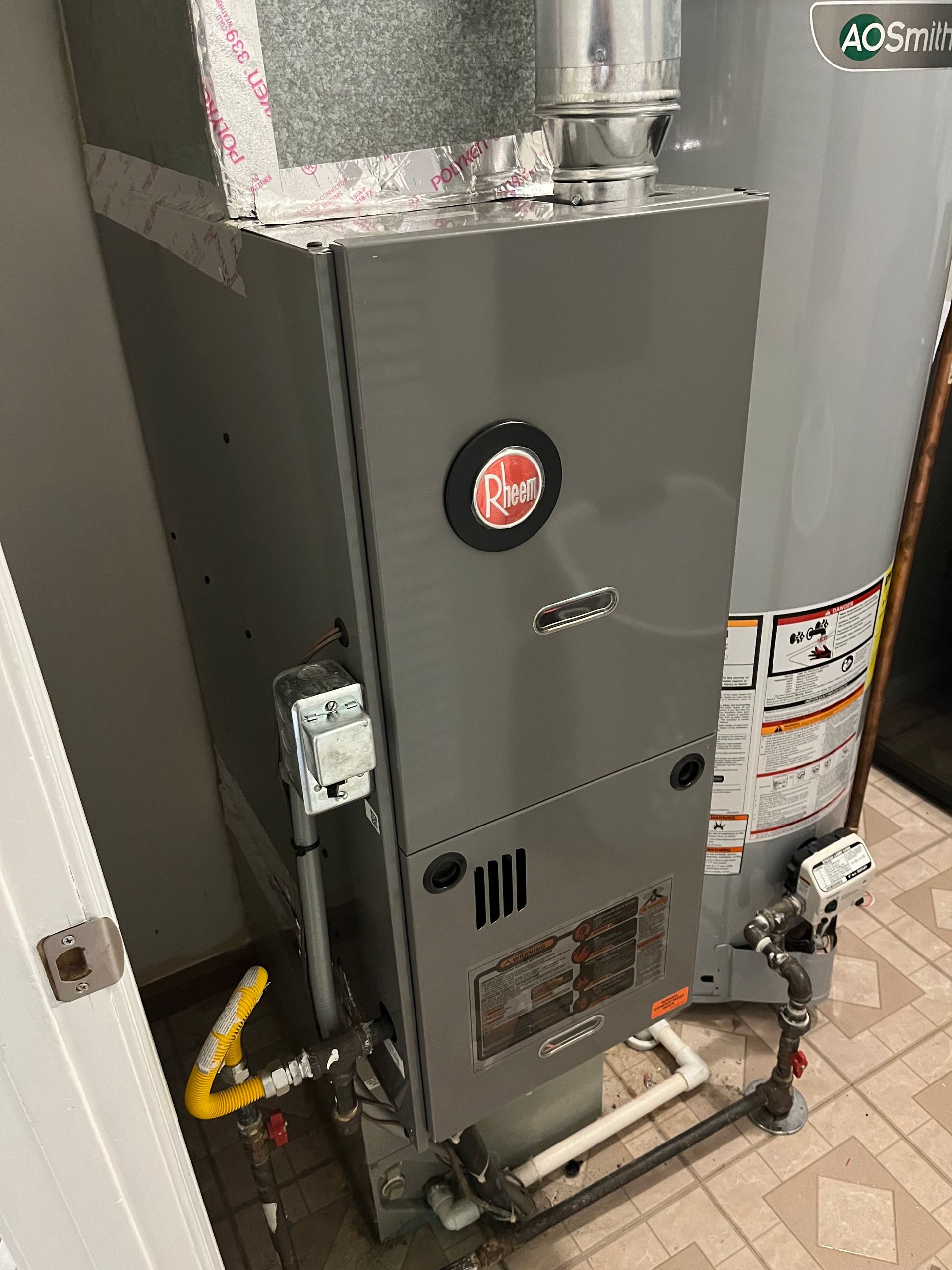 Gray Rheem furnace next to a silver water heater. Ductwork and gas lines are visible.