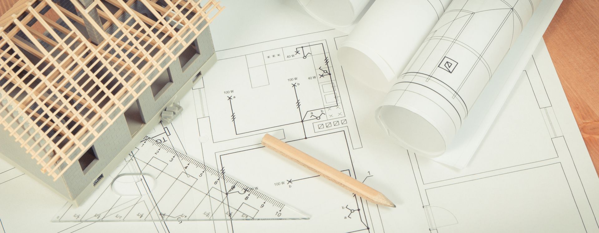 Model house and blueprints on a table with a pencil, illustrating architectural planning and design.