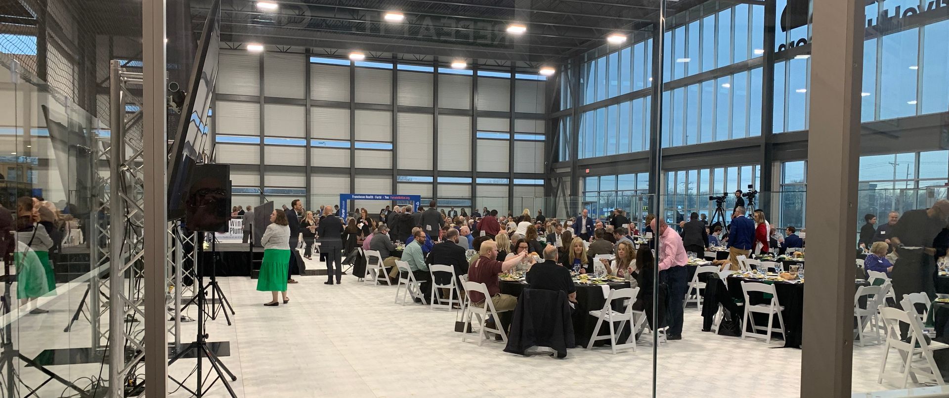 People at tables in large room with tall windows.