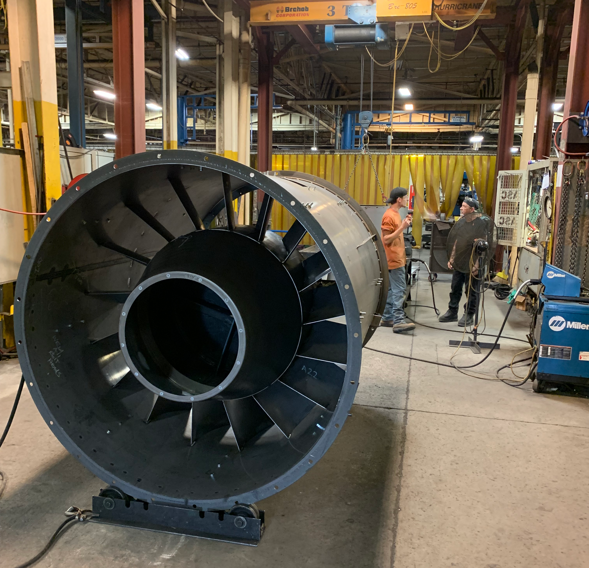 Large industrial fan on a stand, two workers in a factory setting.