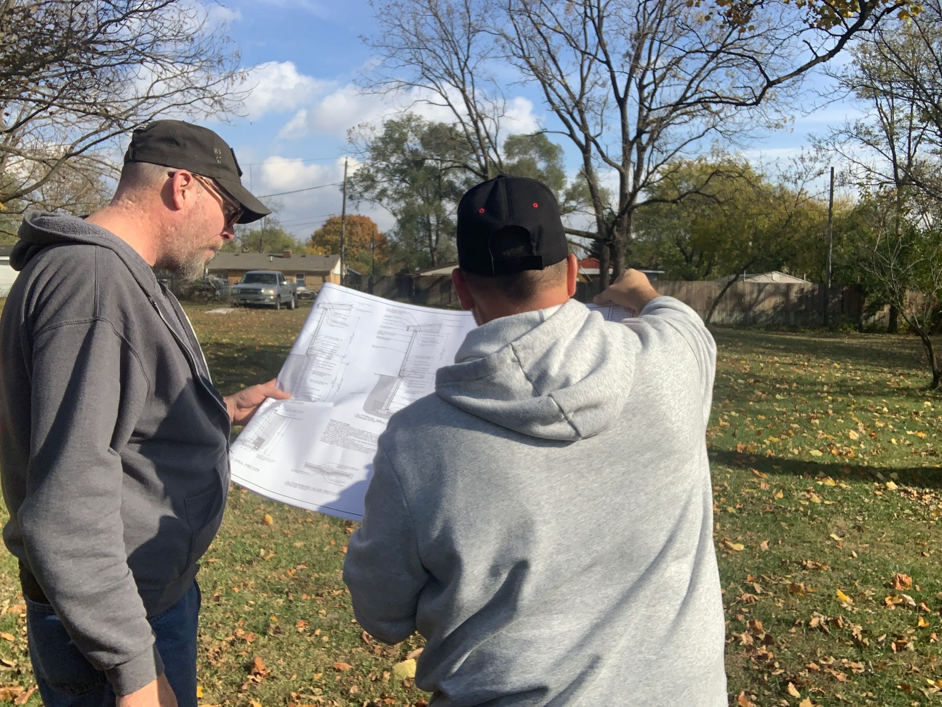 Two men in casual attire examining blueprints outdoors.